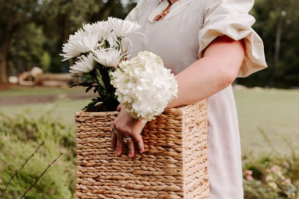 Woman holding a woven basket filled with white flowers outdoors
