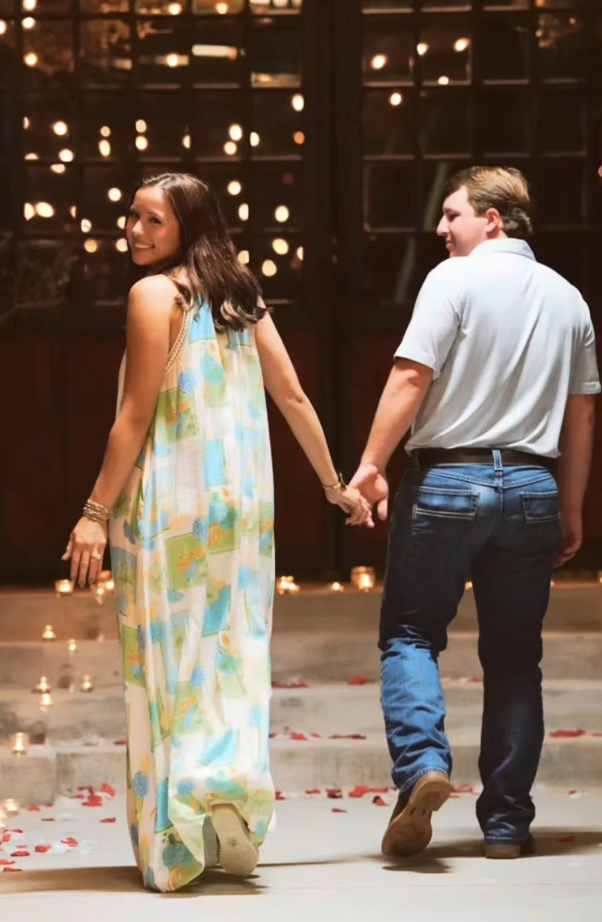 Couple holding hands and walking through a candlelit room scattered with rose petals