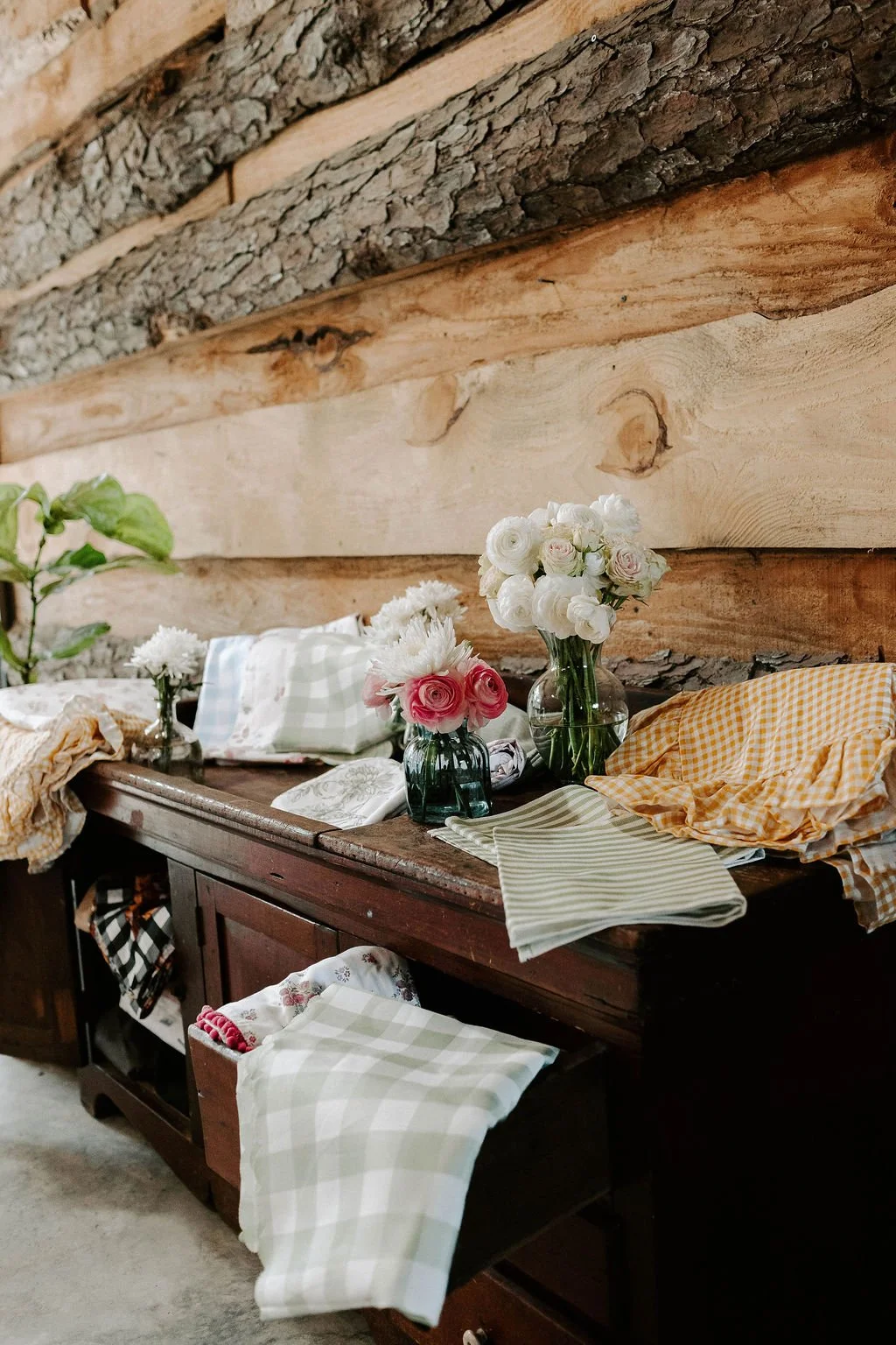 Rustic wooden sideboard decorated with flower bouquets, folded gingham linens, and greenery