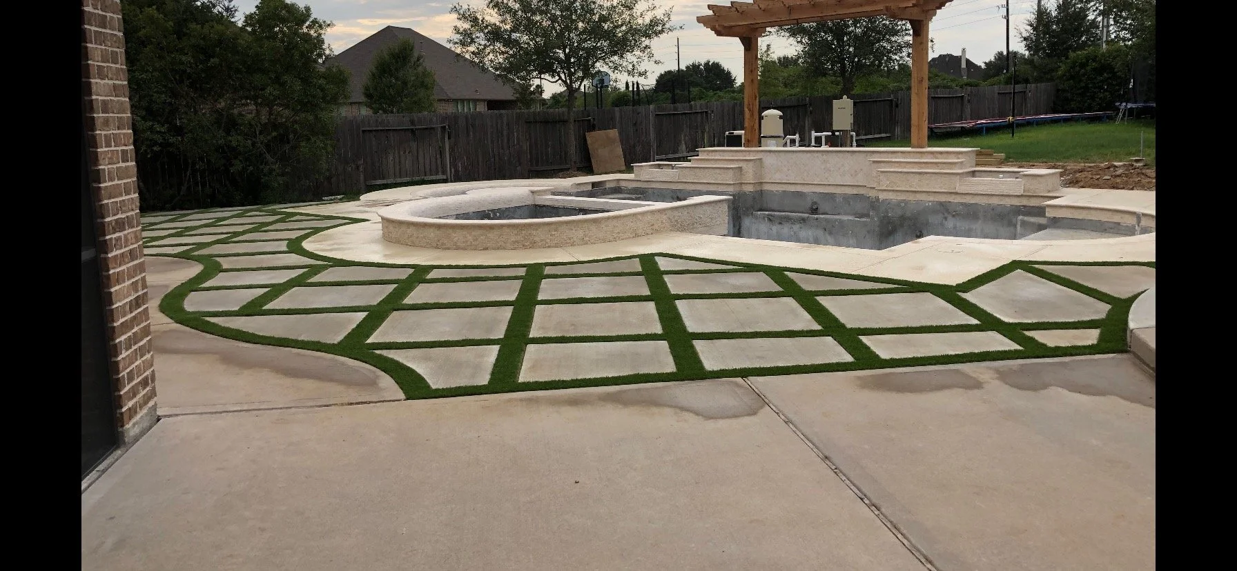 Backyard patio with geometric concrete and artificial turf, a built-in pool, hot tub, and a wooden pergola over a bar area, enclosed by a wooden fence.