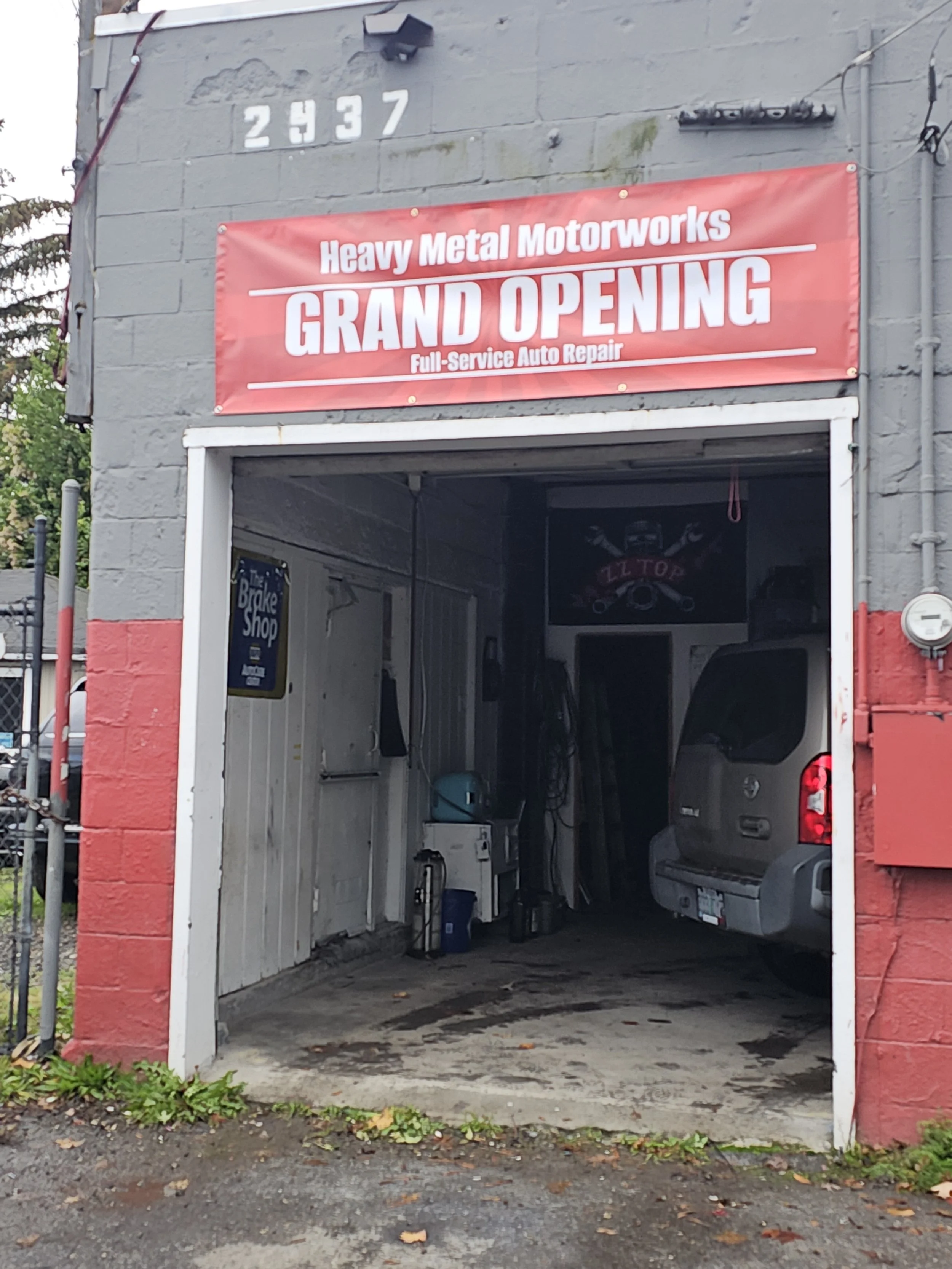 Garage with a sign announcing the grand opening of Heavy Metal Motorworks, a full-service auto repair shop, with a gray vehicle parked inside.