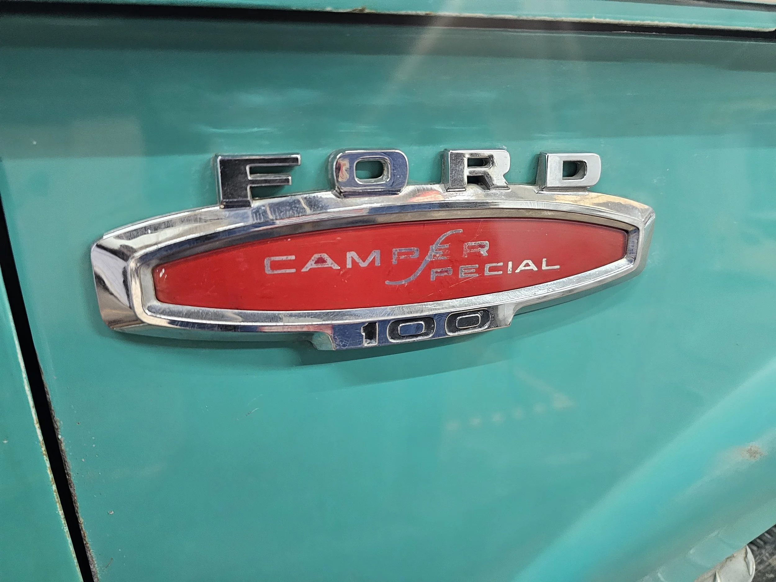 Close-up of a vintage Ford truck emblem reading 'Ford Camper Special 100' on a green vehicle.