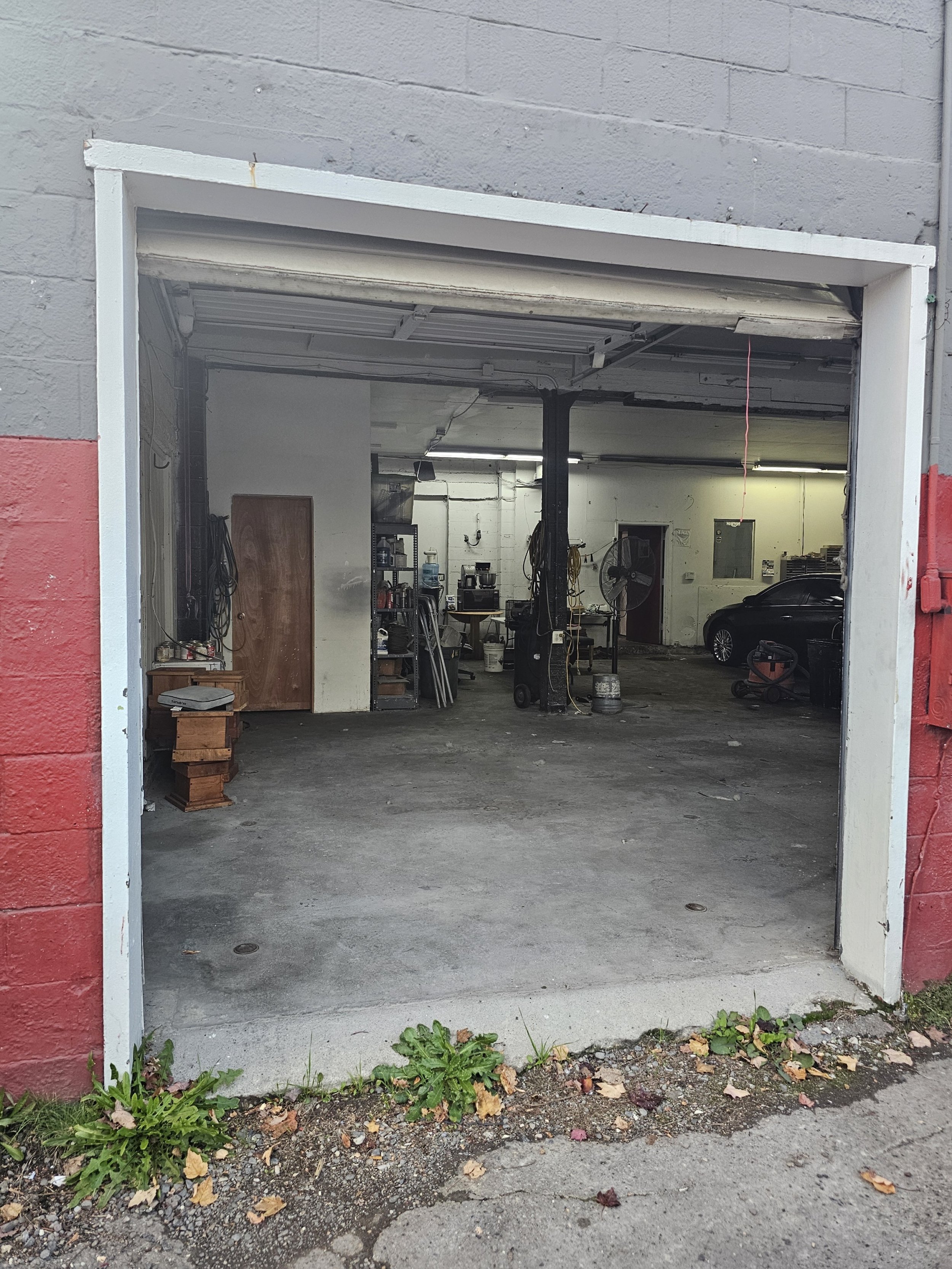 Interior of an open garage with tools, a black car, and various equipment inside.
