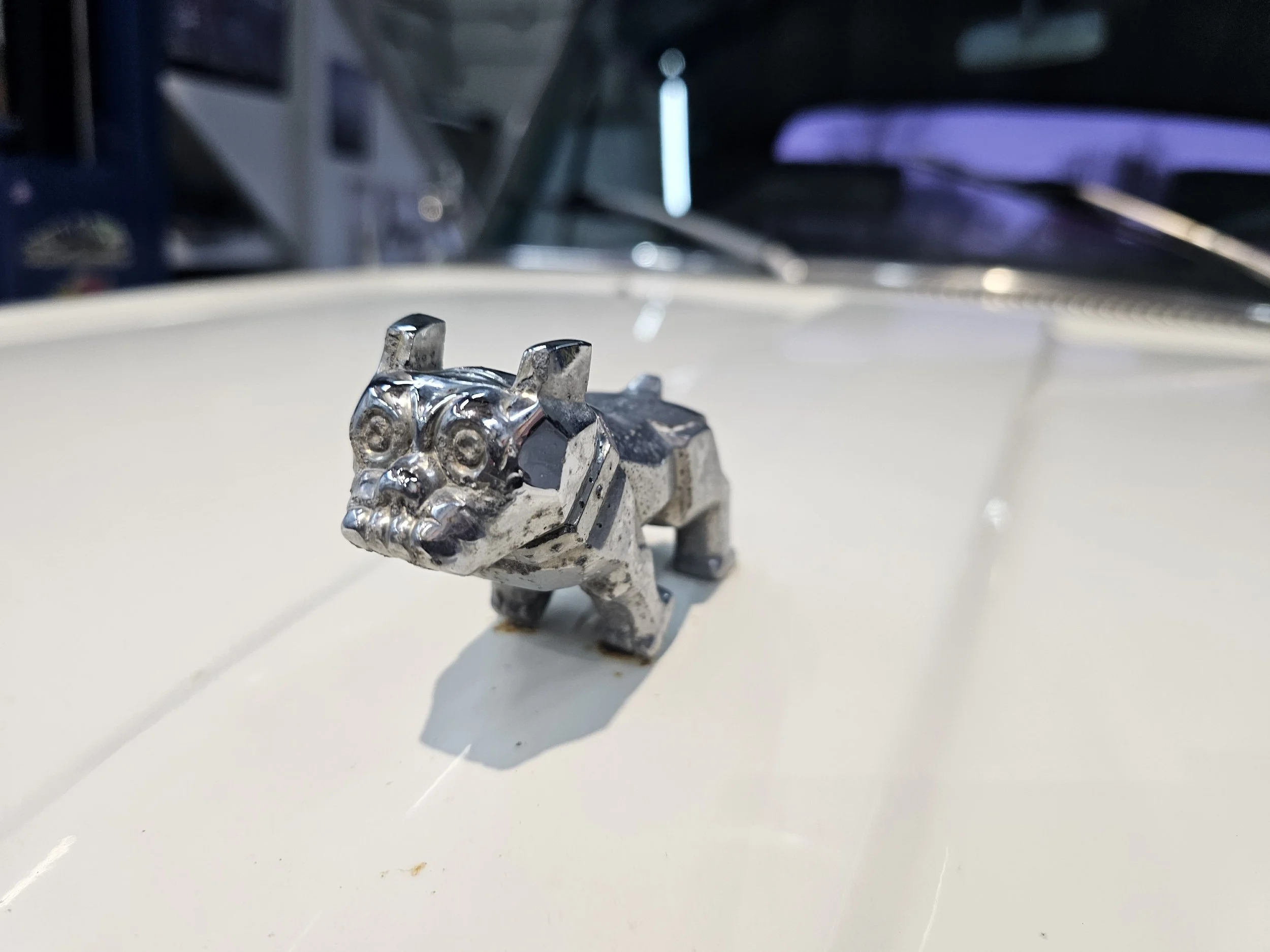 Small silver bulldog figurine on a white surface with a blurred background.