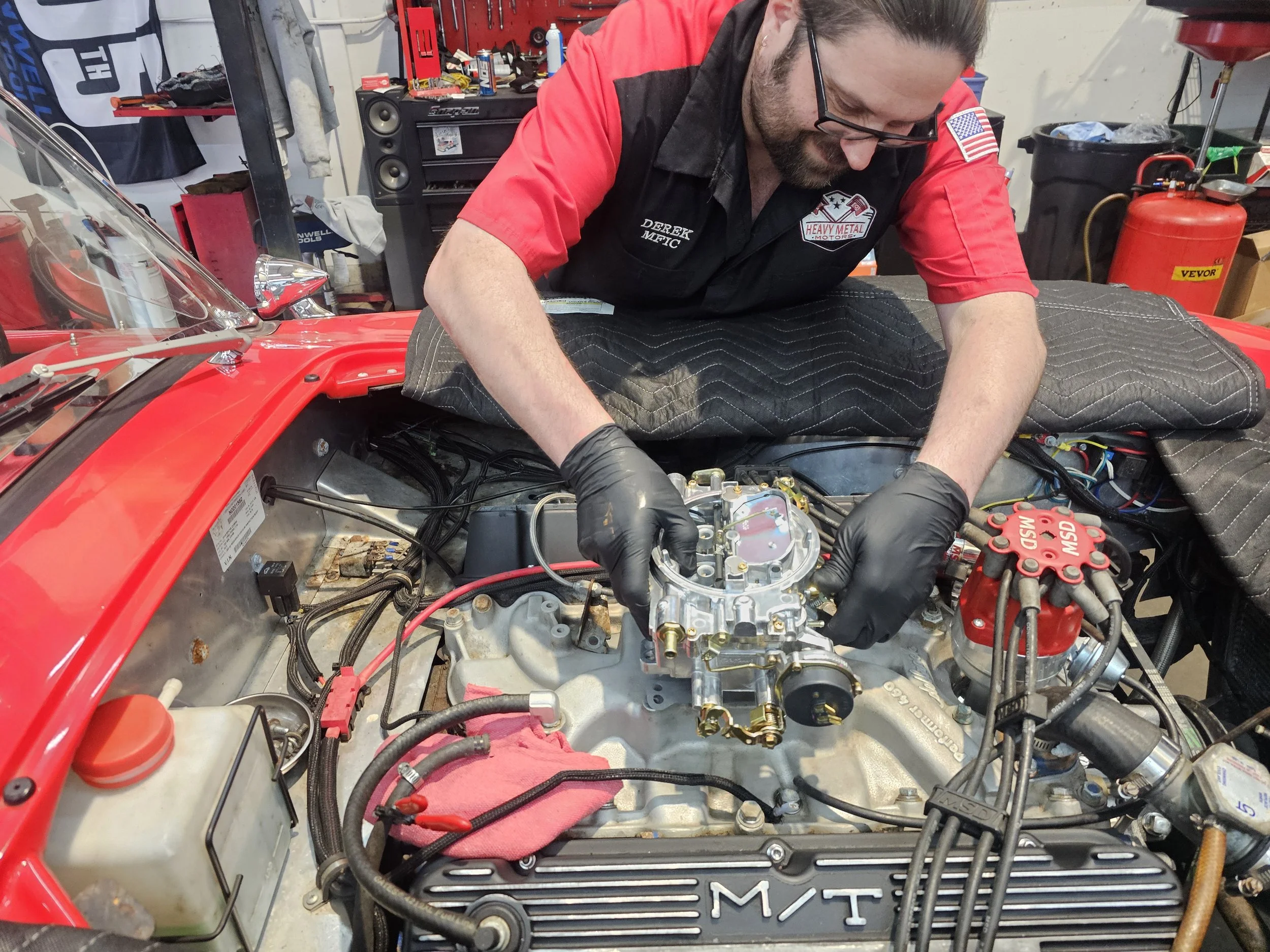 A man with glasses is smiling and inspecting an Edelbrock caburetor on a Ford 460 V8 Big Block Engine