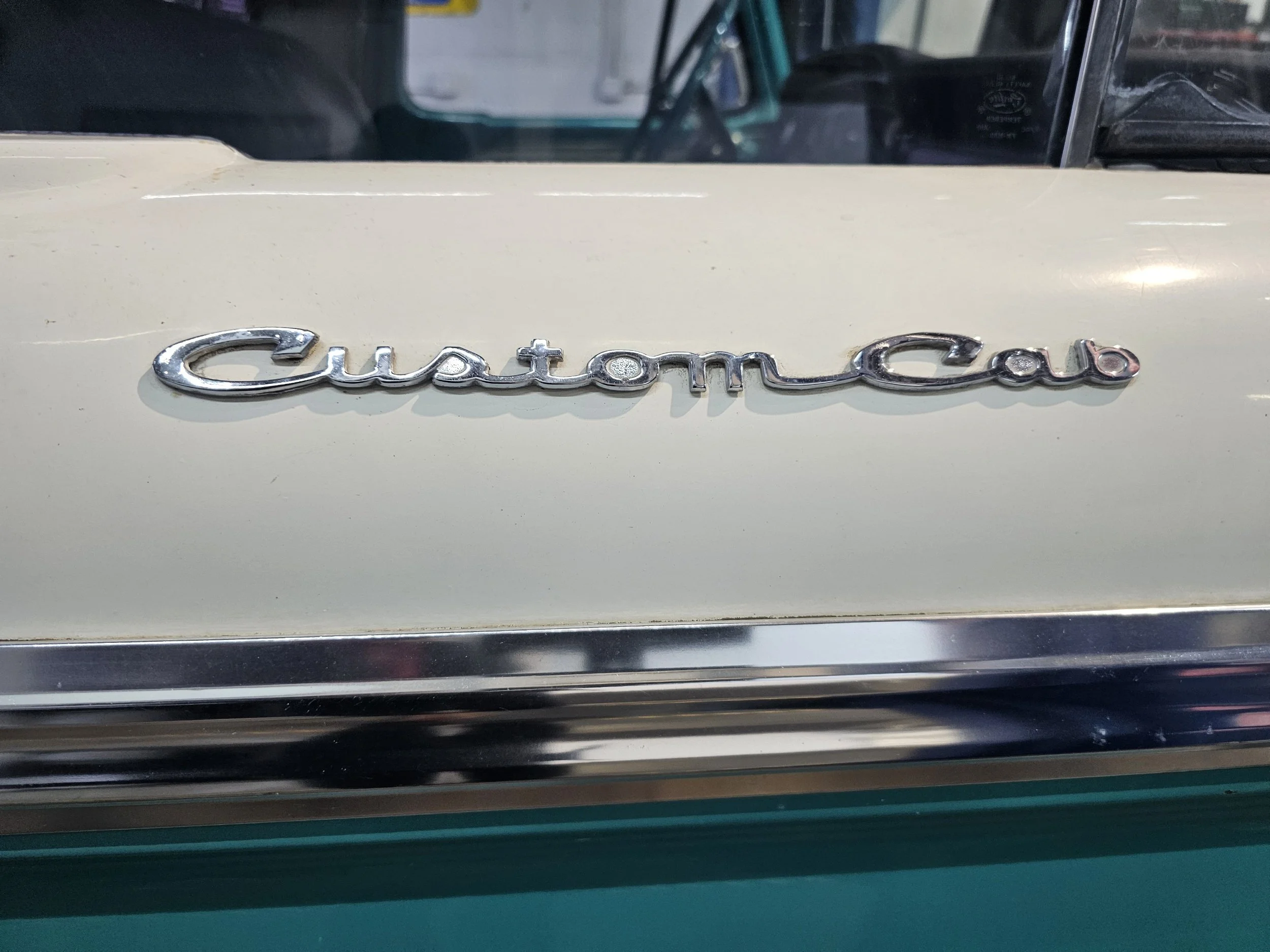 Close-up of a car with a chrome emblem that reads 'Custom Auto' on a cream-colored surface.
