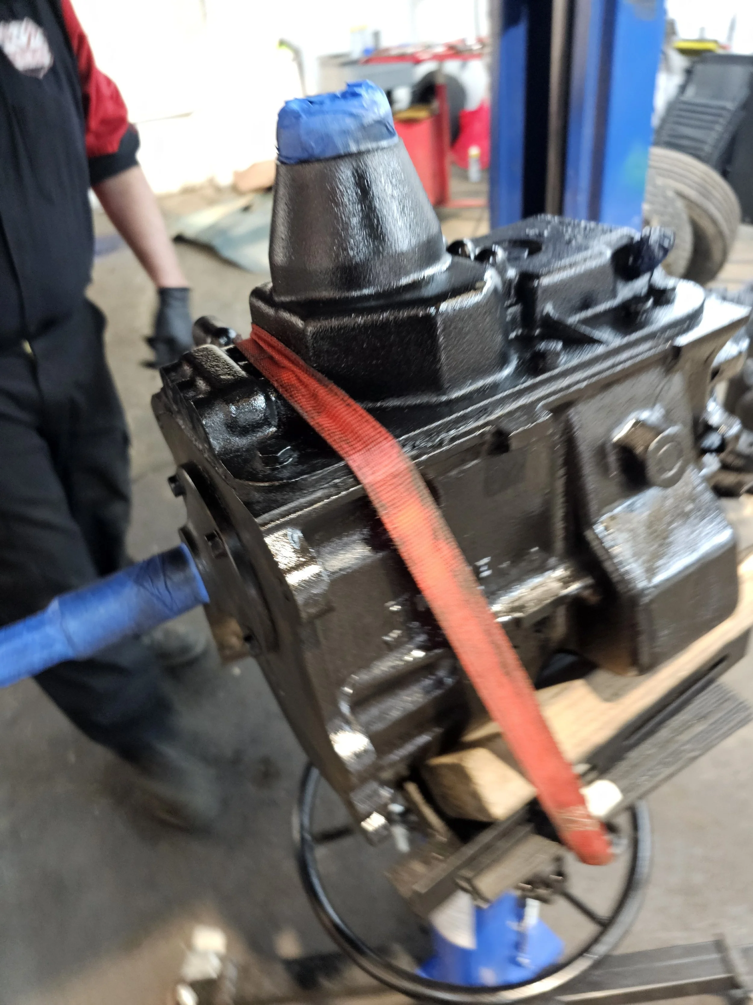 A black engine block secured with a red strap on a workbench in a garage.