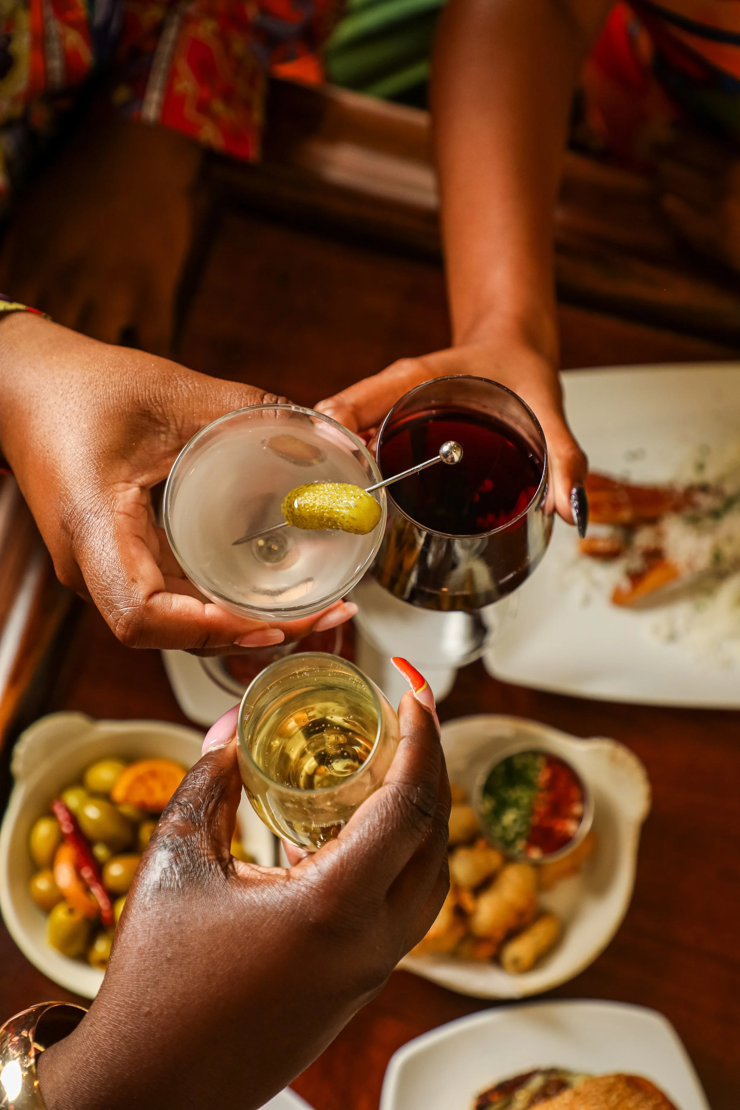 People toasting with glasses of wine and champagne at a gathering with various dishes of food on a table.