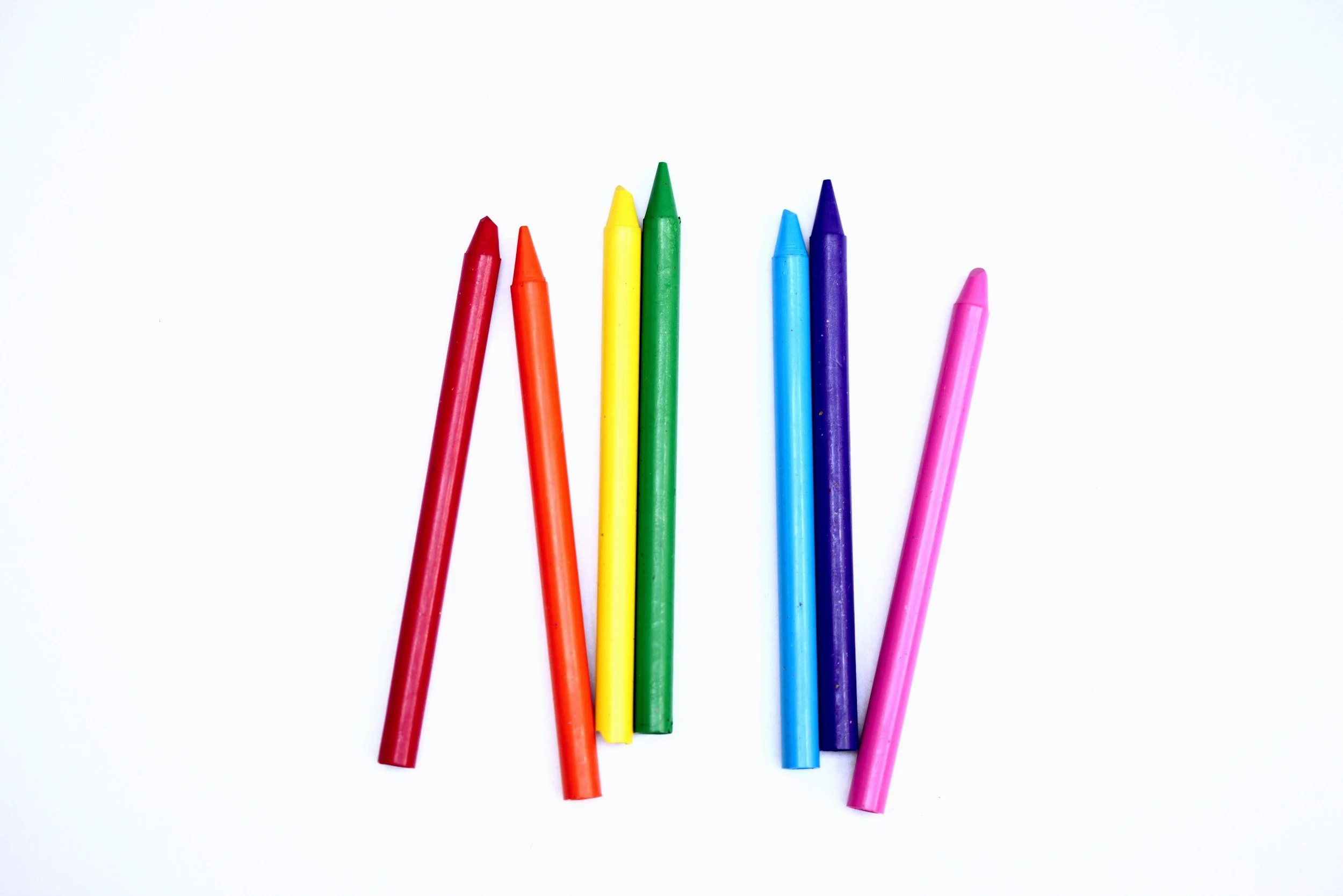 Six colorful crayons: red, orange, yellow, green, blue, purple, and pink on a white background.