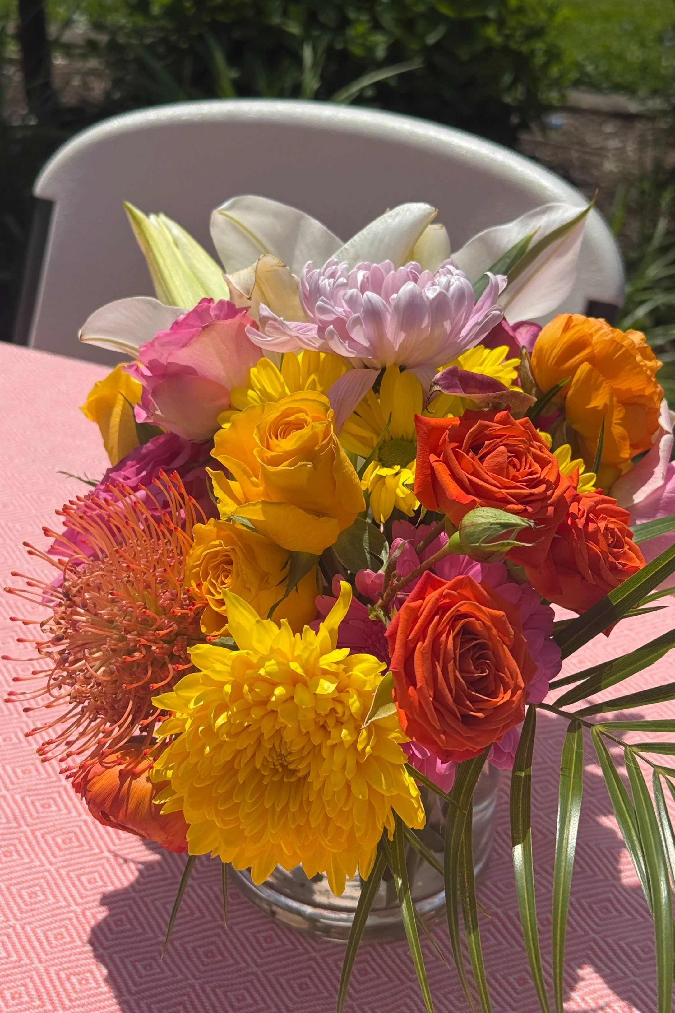 Outdoor tropical floral arrangement featuring roses, protea, lilies, and lush greenery in vivid orange, pink, yellow, and green hues — designed by Beam & Bramble for a Hawaiian-inspired celebration