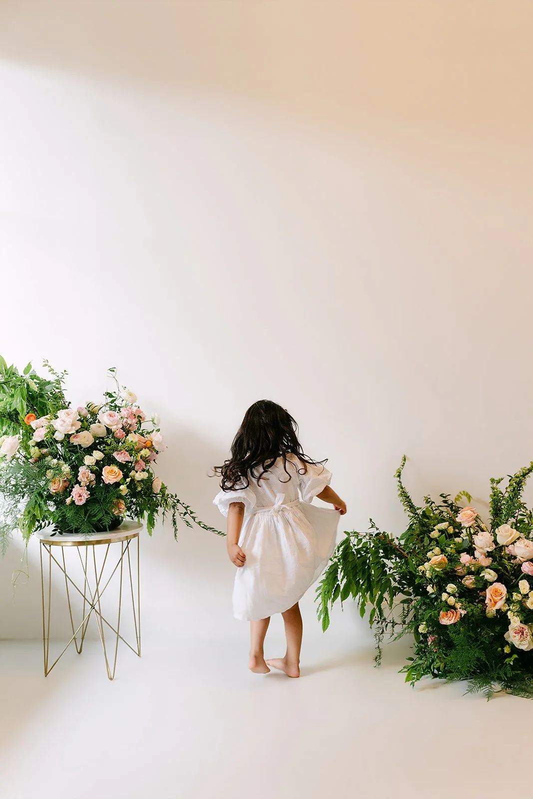 Photo of floral arrangement in photoshoot, little girl turned away with long hair and white dress, taken by Crystal Chavez Photo