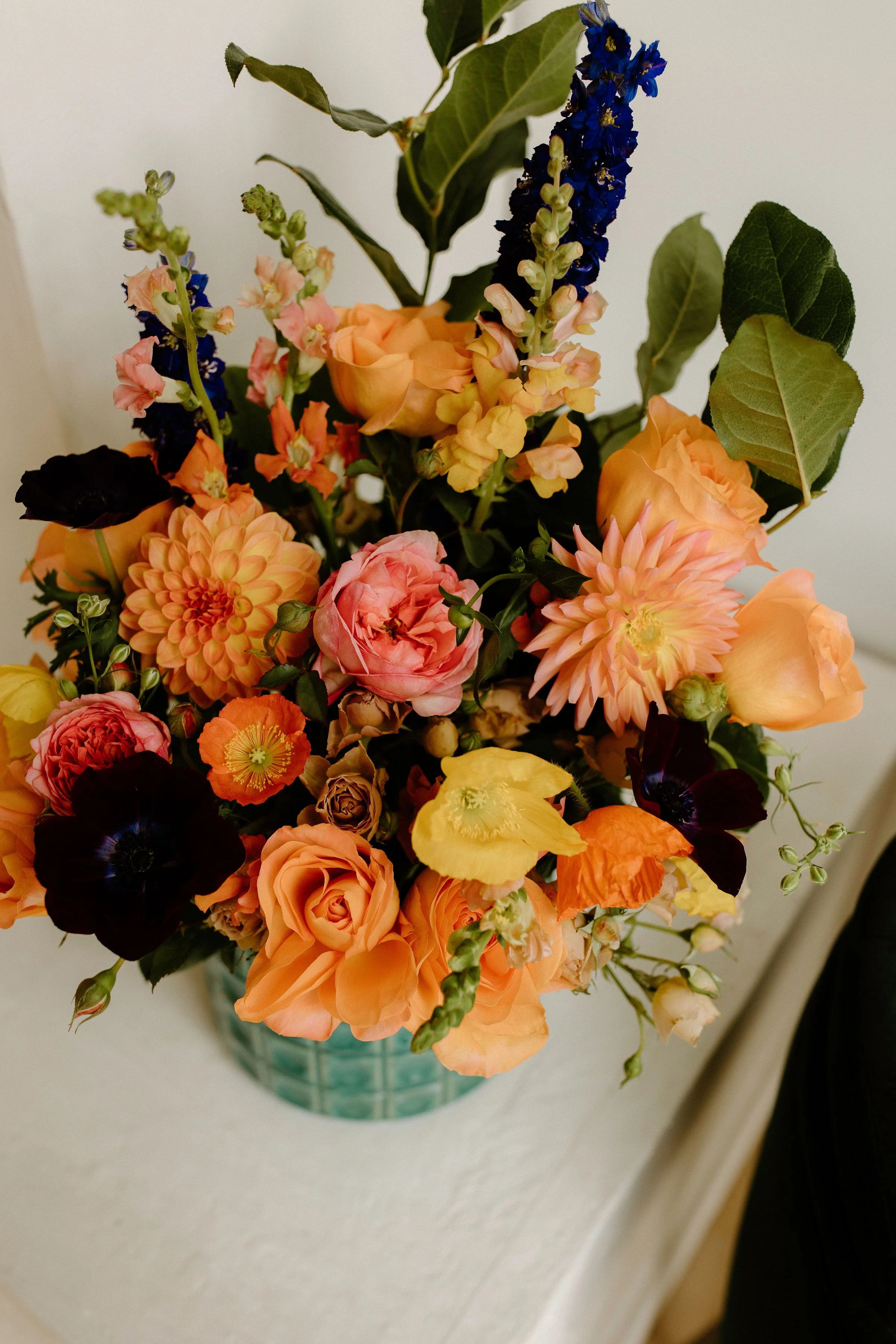 Editorial floral arrangement in a teal vessel, featuring jewel-toned blooms like orange california poppies, blush roses, and deep burgundy scabiosa — ideal for brand and content styling.