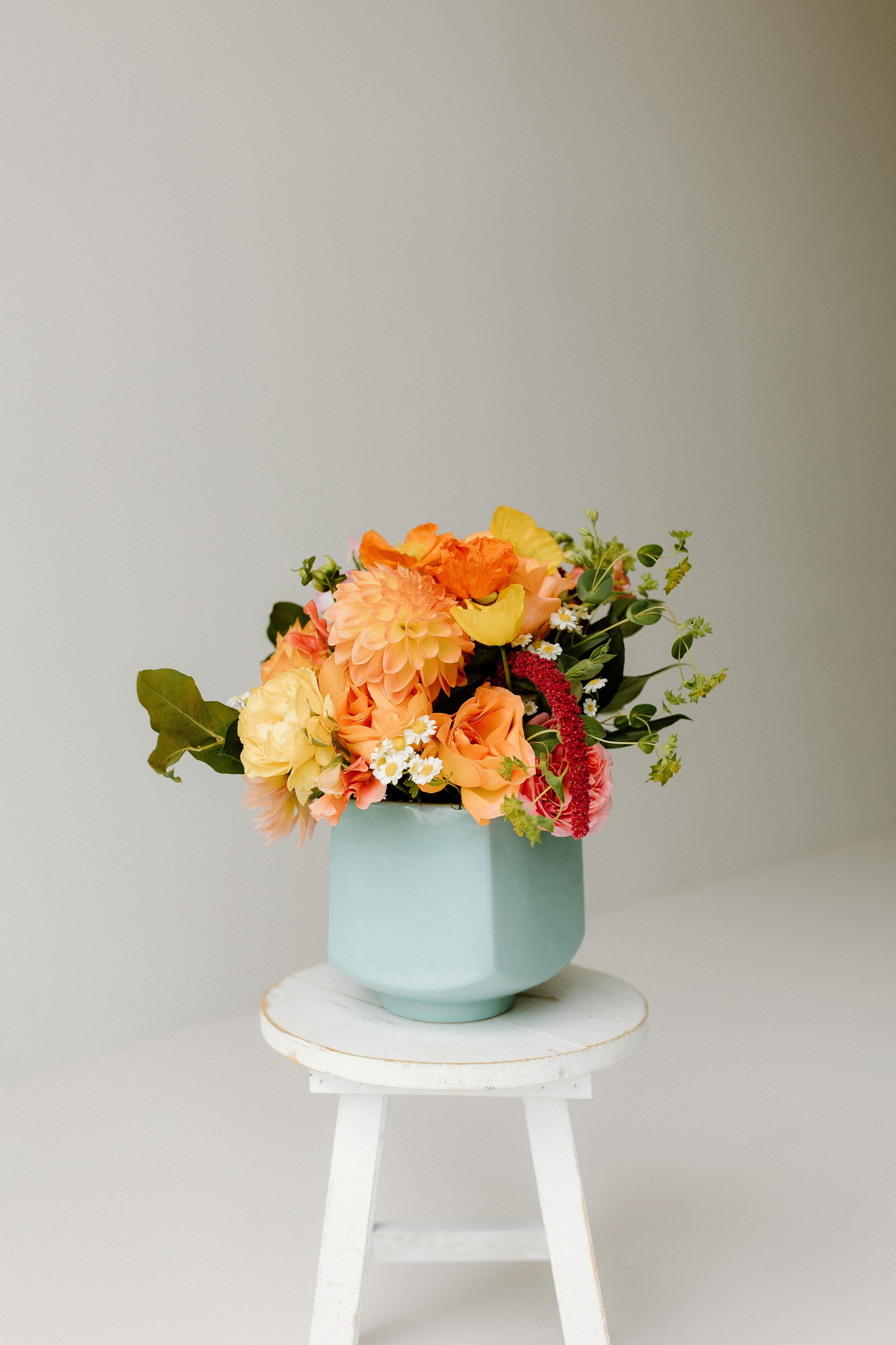 Classic Golden Hour bouquet featuring blush roses, bright greens, and textured florals in a balanced, sculptural arrangement with a soft powder teal blue ceramic vase with organic and modern lines