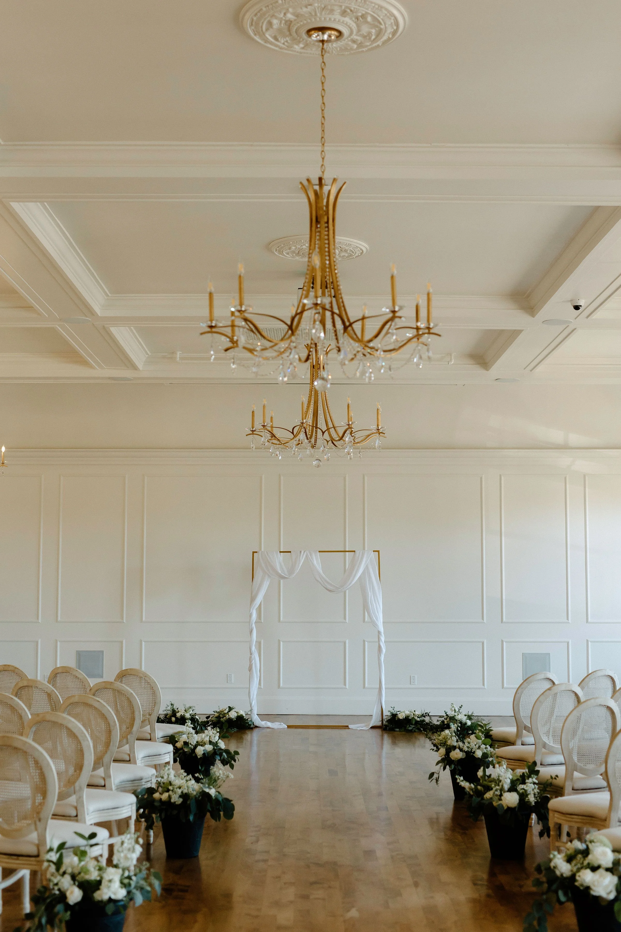 Wedding aisle featuring a simple golden rectangular arch draped in white chiffon, with custom running aisle bouquets — a refined and romantic Beam & Bramble ceremony design
