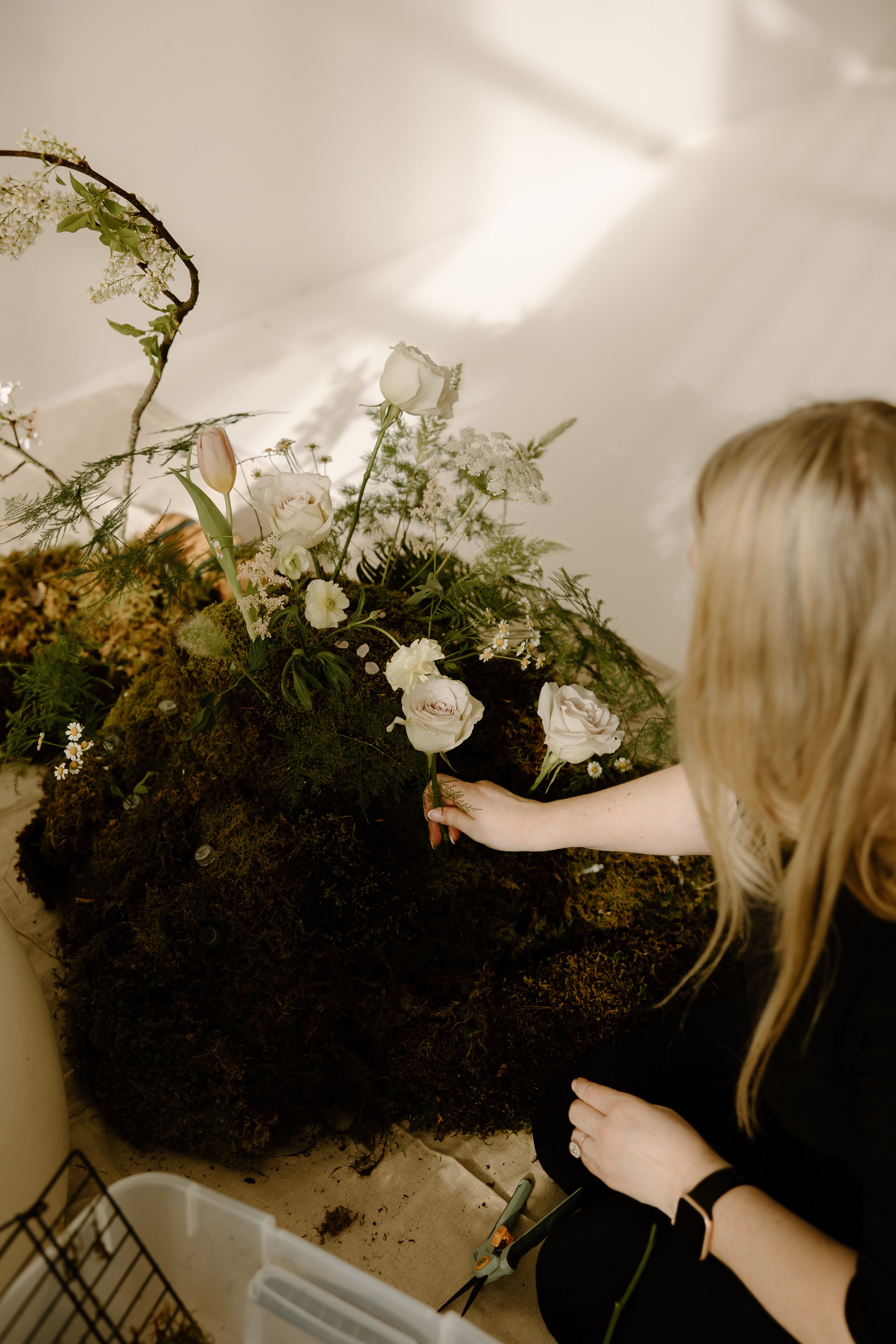 Floral designer Amber Engelhardt placing botanicals within a moss-covered floor installation created for an editorial photoshoot in Portland, Oregon. Photo by Kay Gilgan Photography.