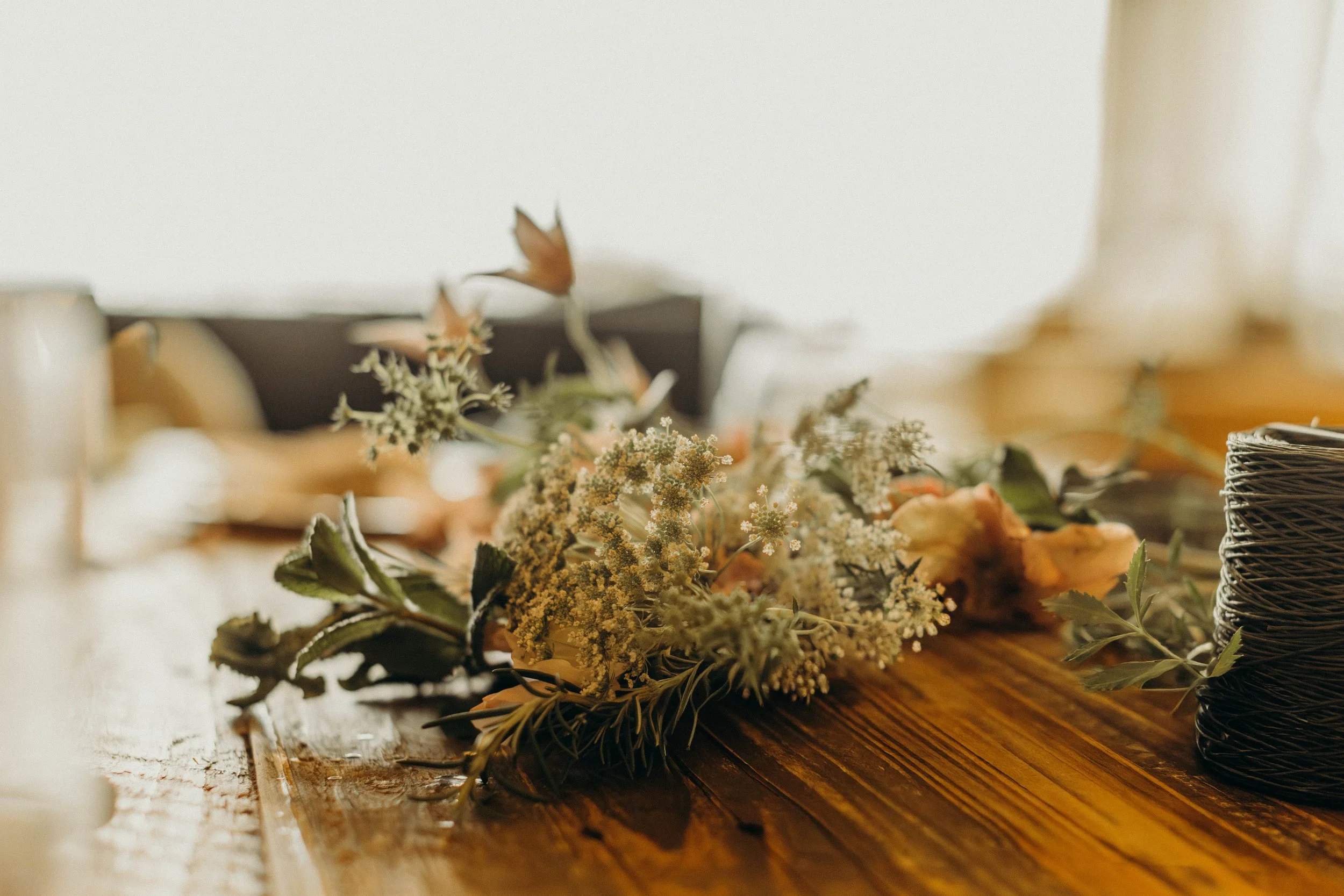 Decorative arrangement of small white flowers and green leaves on a wooden table, with blurred background, captured by Alison May Photography.