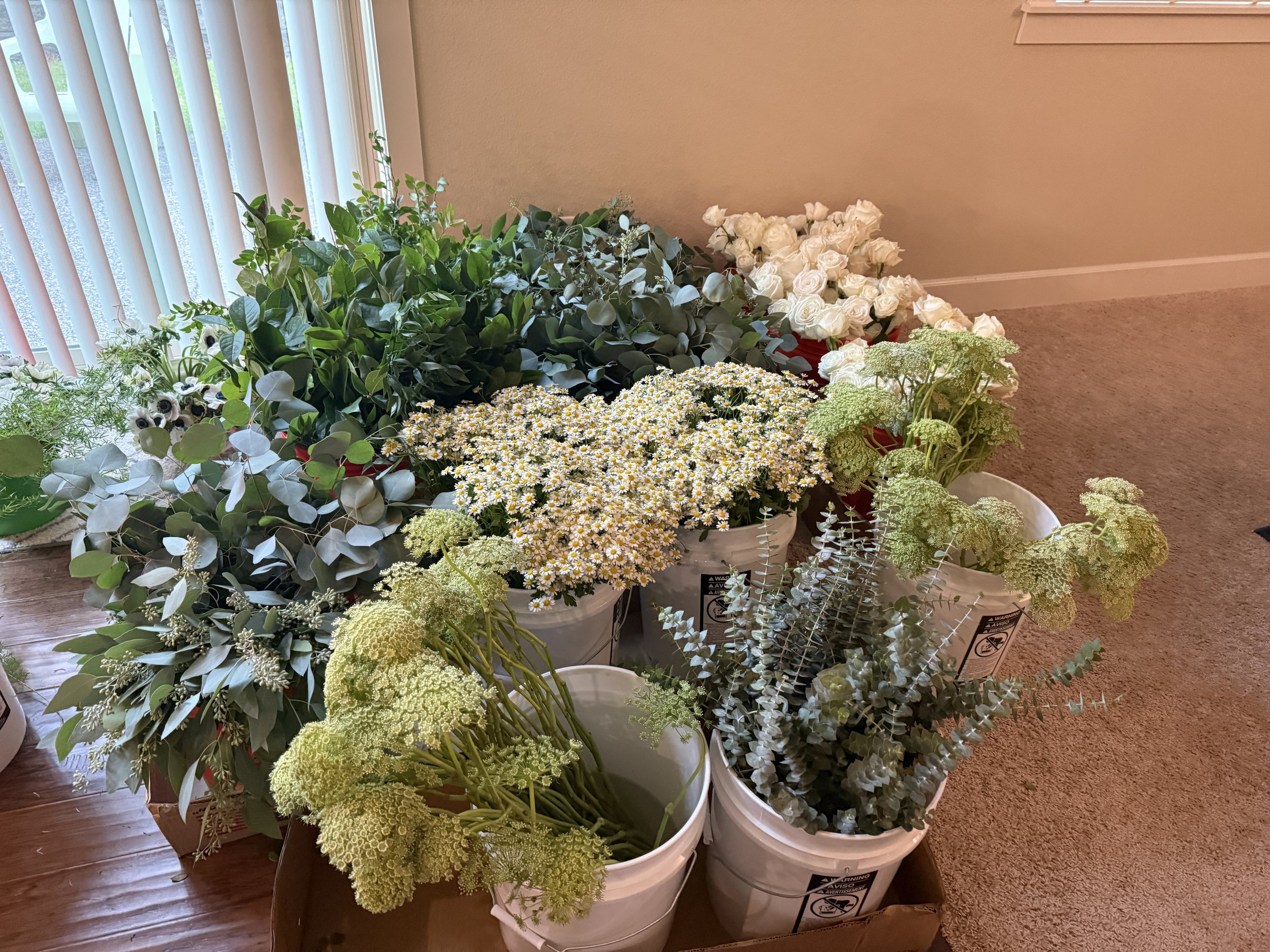 Buckets filled with fresh greenery, chamomile, Queen Anne’s lace, and seasonal filler flowers prepared for a Bloom Bar floral arranging event