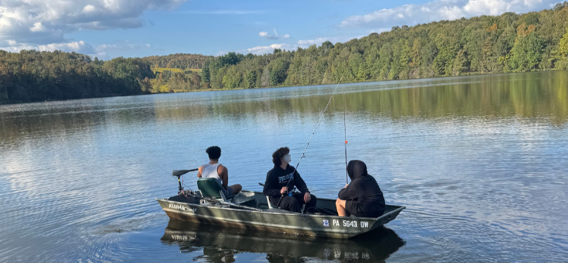 Residents fish from a small boat on a calm lake during a fall recreation outing.