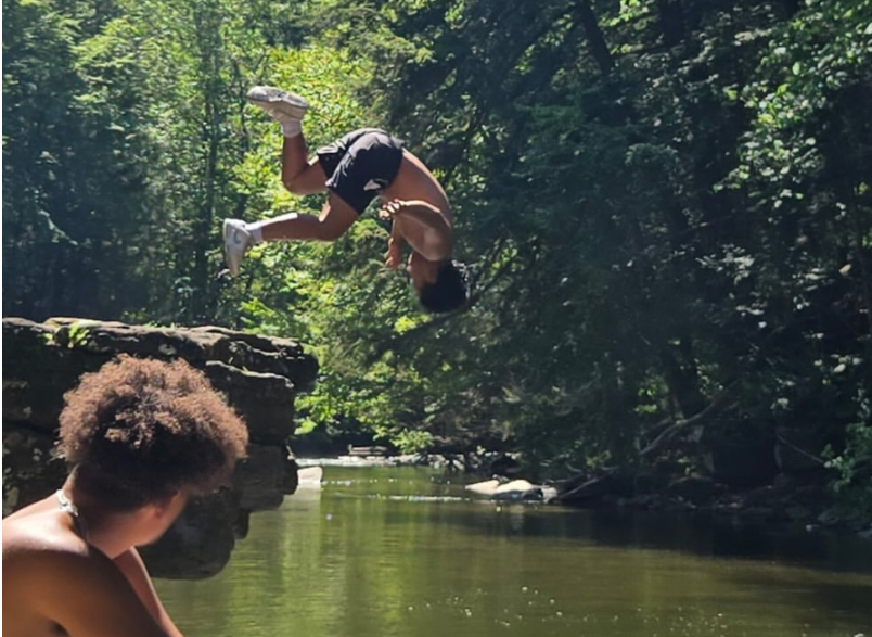 A resident does a backflip into a creek while peers watch during a supervised summer outing.