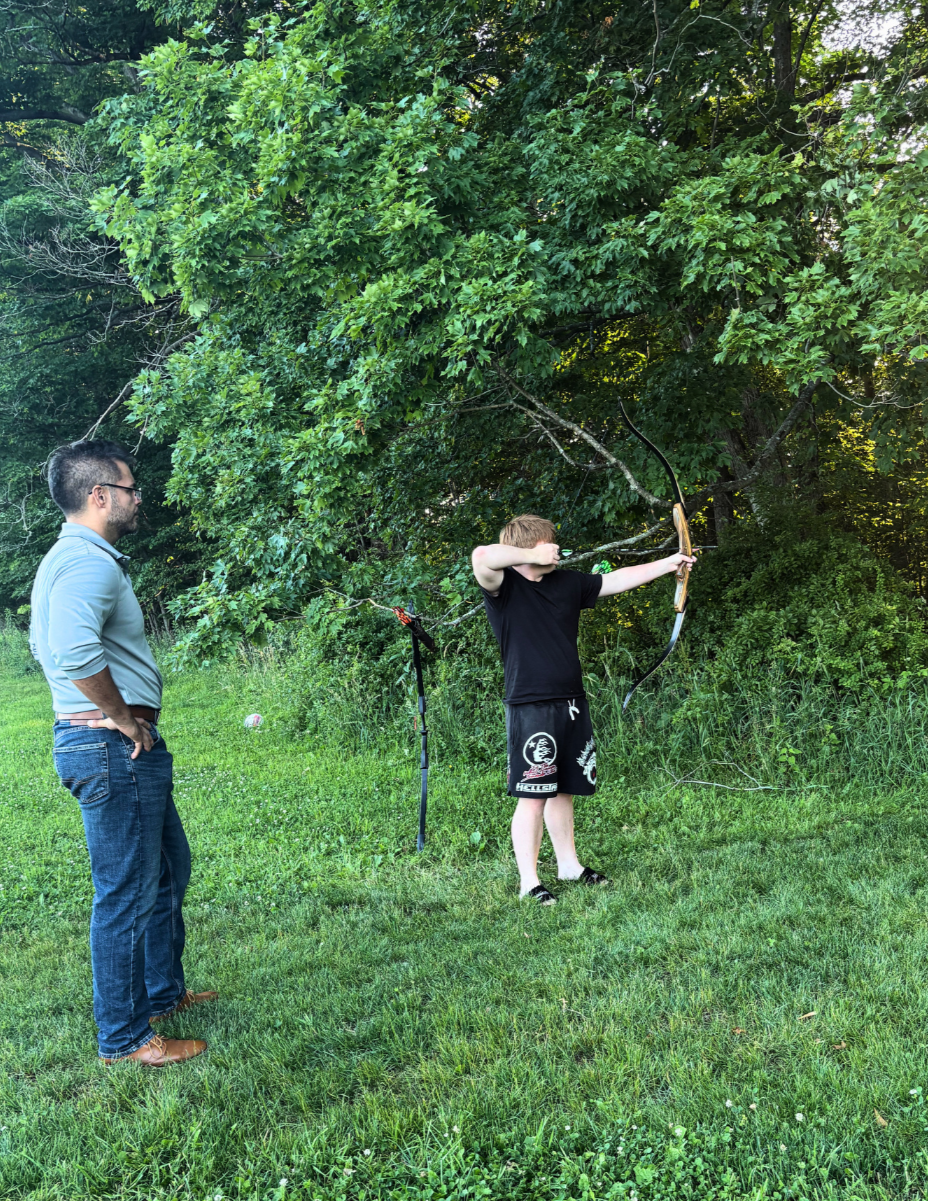 Woodhaven resident practicing archery outdoors with staff support during a summer activity