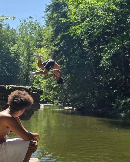 Teen jumping into a creek during a favorite Woodhaven Recovery summer recreation outing while peers enjoy the outdoors.
