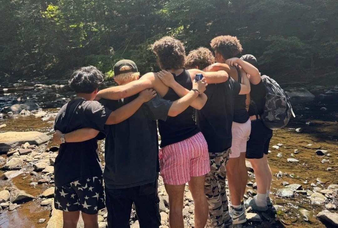 Teen boys at Woodhaven Recovery standing together with arms around one another beside a creek, demonstrating the fellowship, connection, and peer support that strengthen recovery.