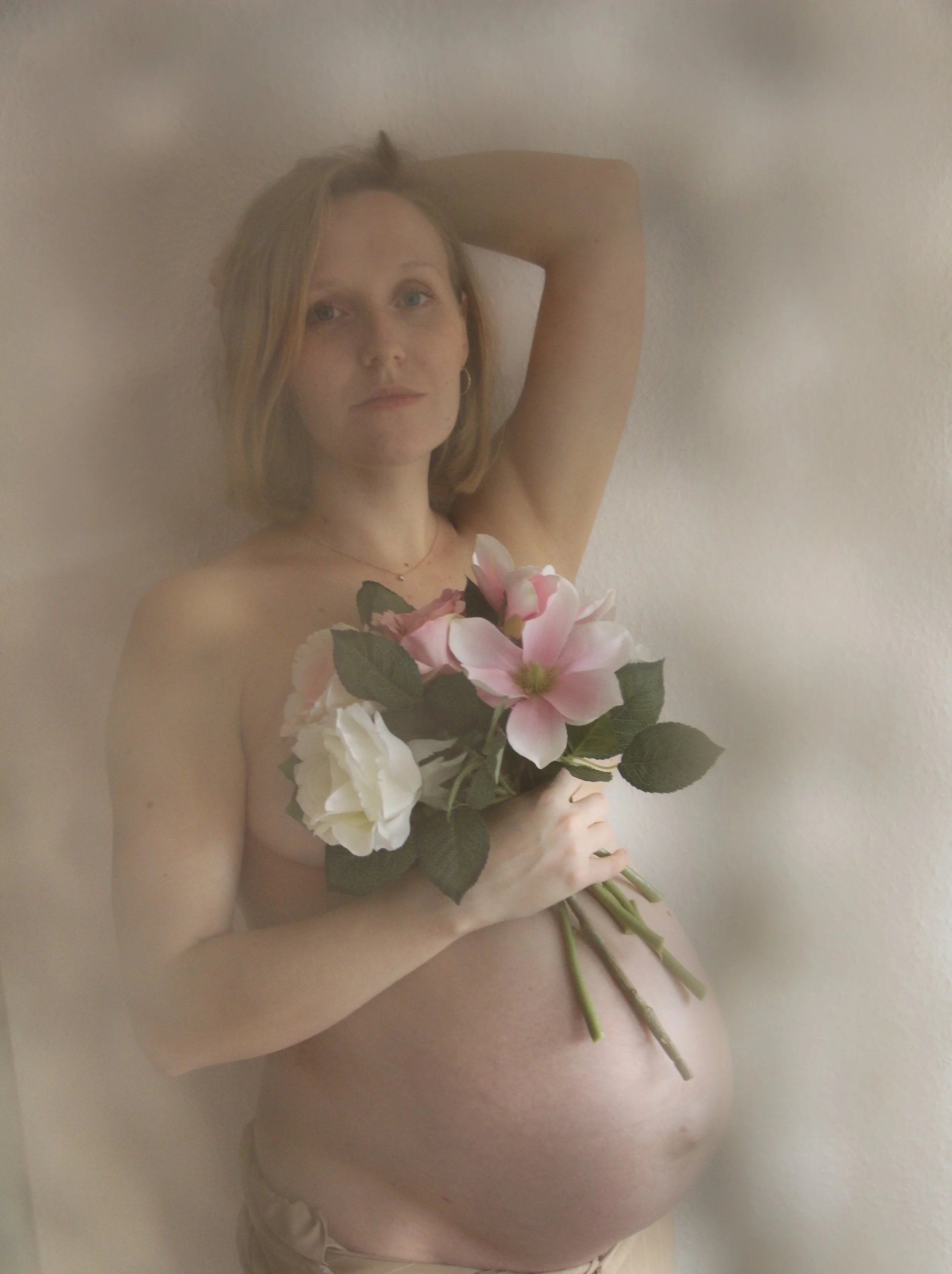 Porträt einer schwangeren Frau im Studio – ruhige Pose und weiches Licht mit Blumenstrauss