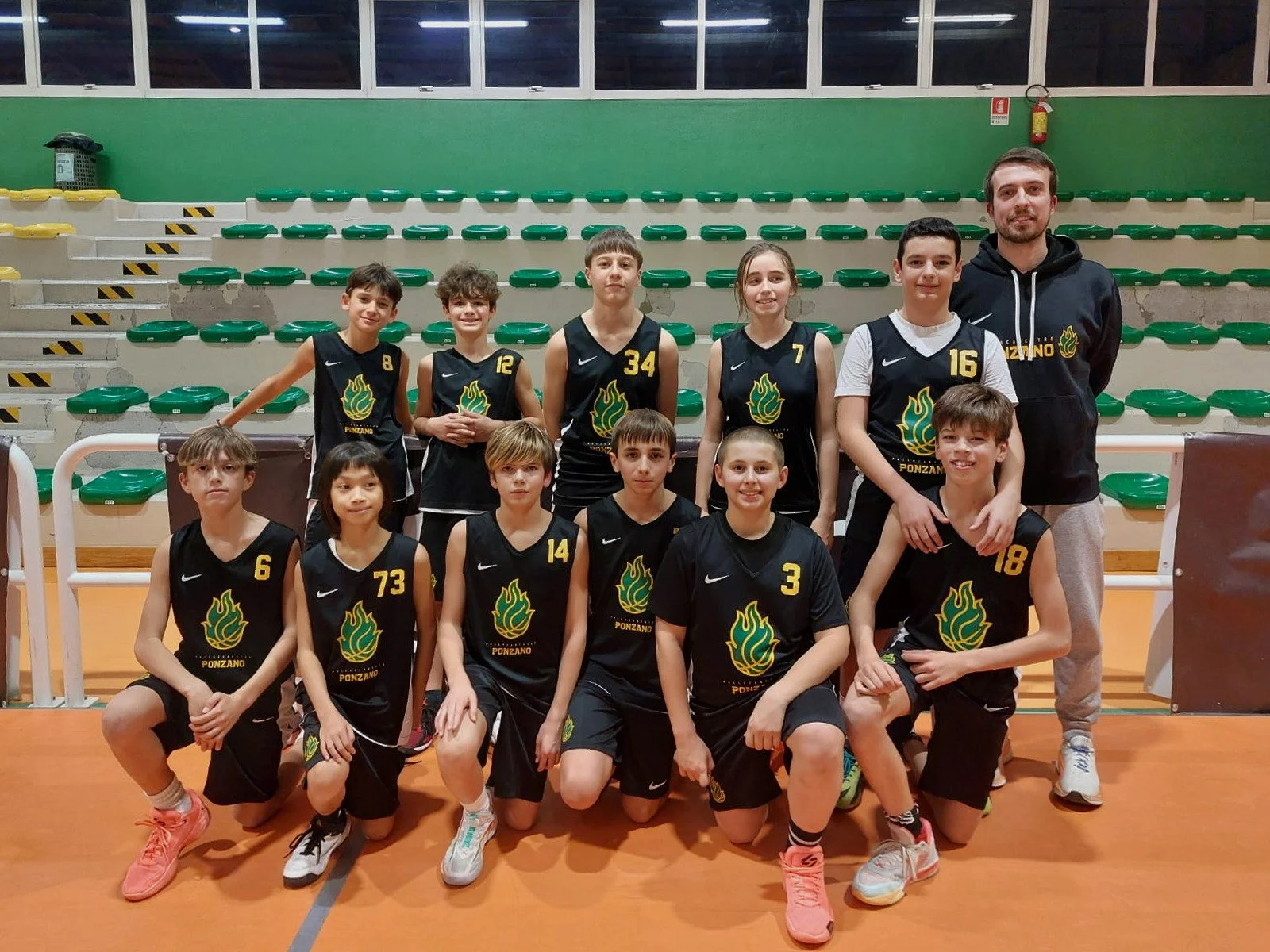 Gruppo di ragazzi e ragazze dell'under 13 maschile della pallacanestro ponzano giovani in uniforme di basket, con un Riccardo Toffolo, in un'arena sportiva.