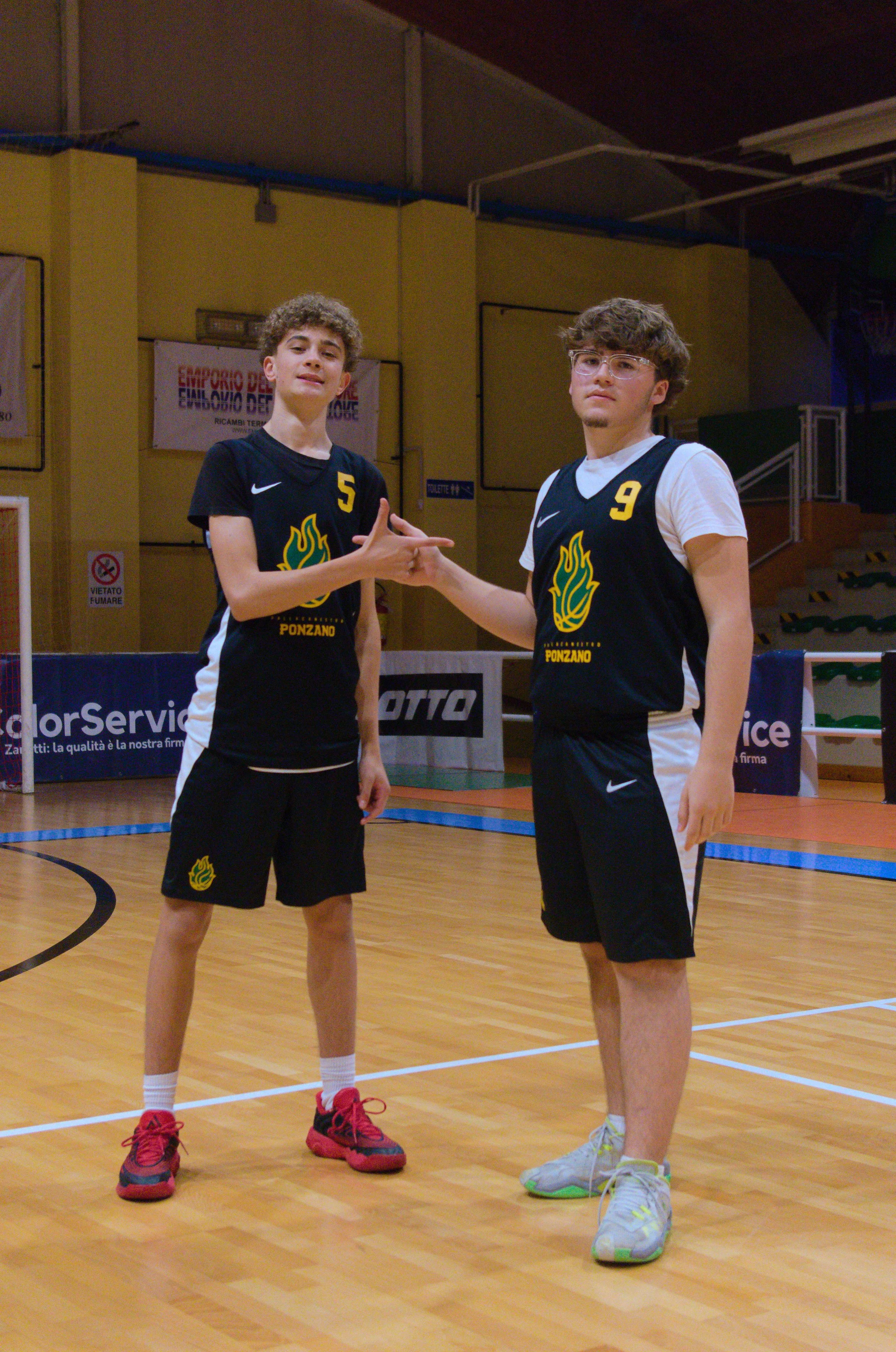 Due giovani giocatori di basket u17 maschile in un campo indoor del Palacicogna si stringono la mano. Indossano divise nere con dettagli bianchi e logo della pallacanestro ponzano, e numeri 5 e 9.