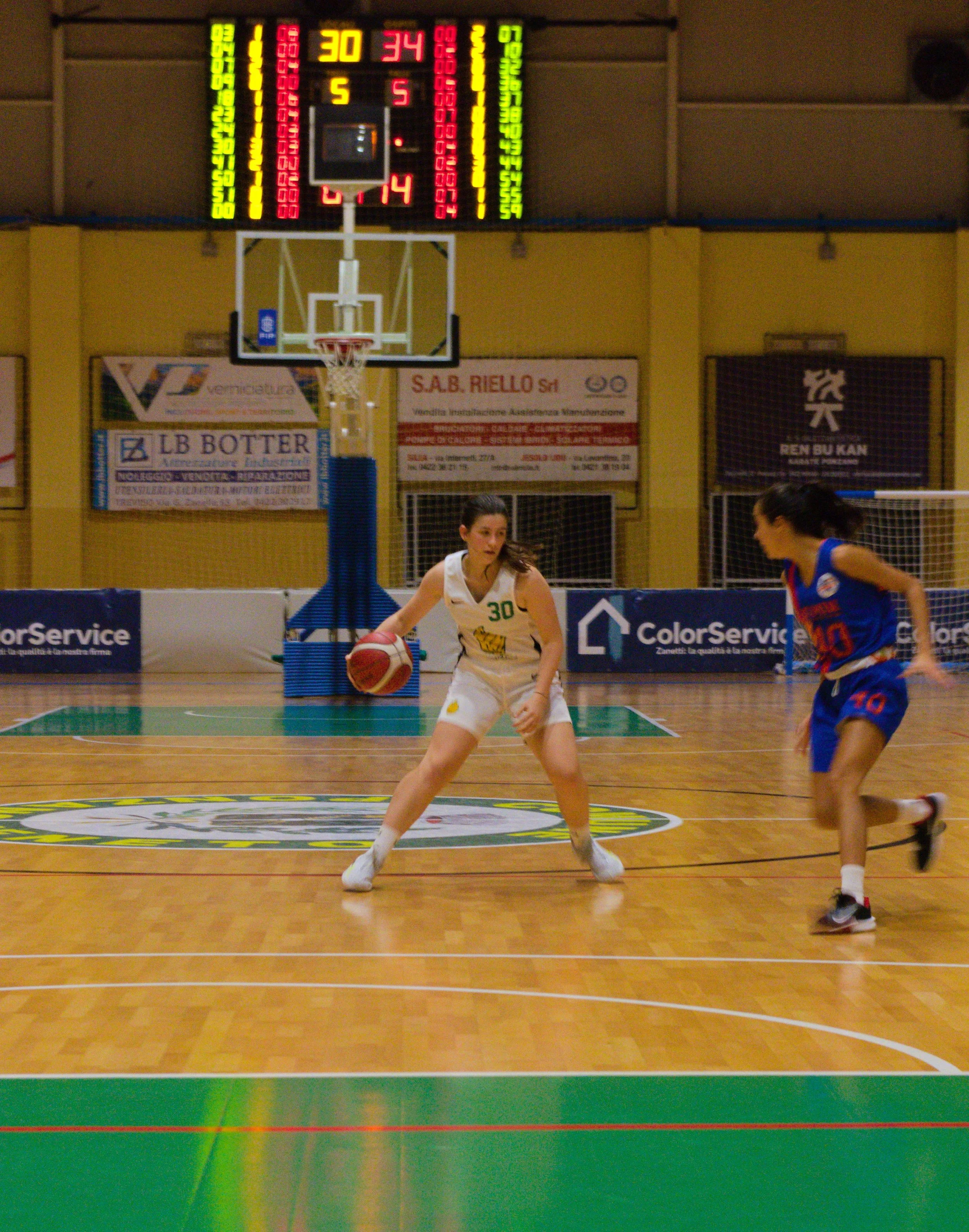 Una giocatrice della promozione della pallacanestro ponzano gioca in un campo di basket, una con la palla e l'altra in posizione difensiva.