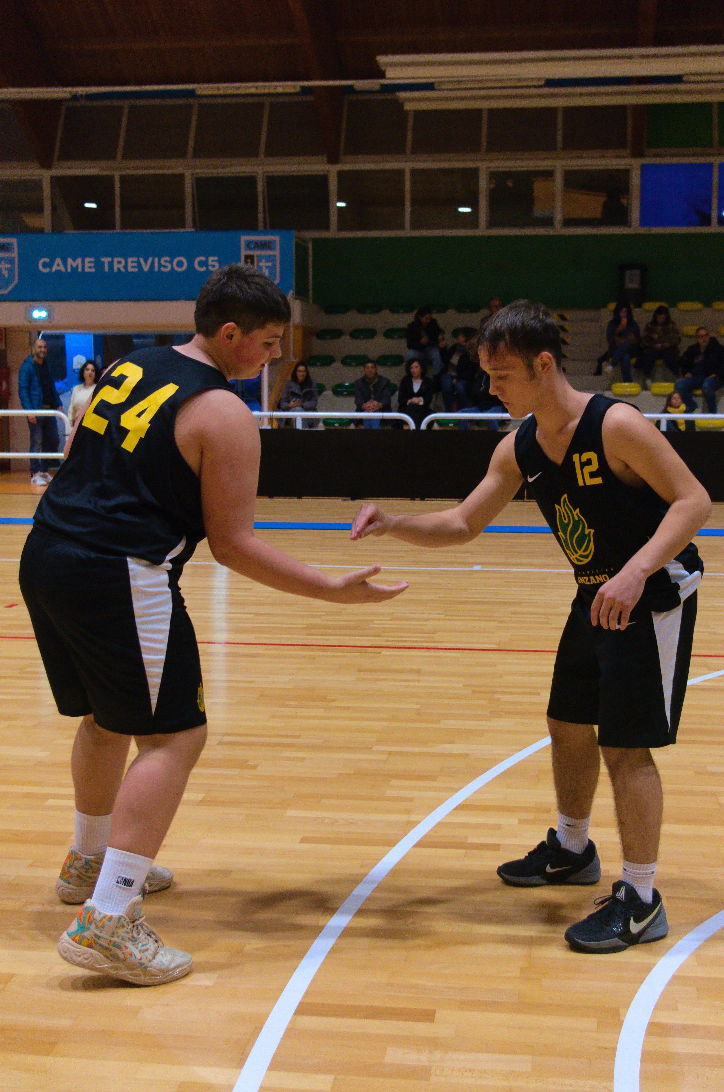 Due giocatori di basket in un campo, uno con il numero 24 e l'altro con il numero 12, si stringono la mano durante una partita.