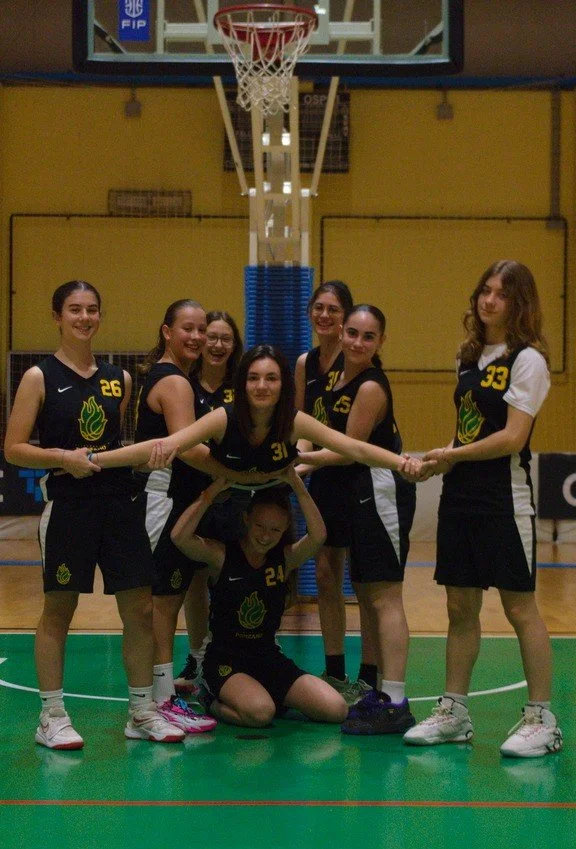 Gruppo di ragazze dell'u14 femminile della pallacanestro ponzano in divisa da basket che si tiene per mano sulla pista del campo da basket indoor.