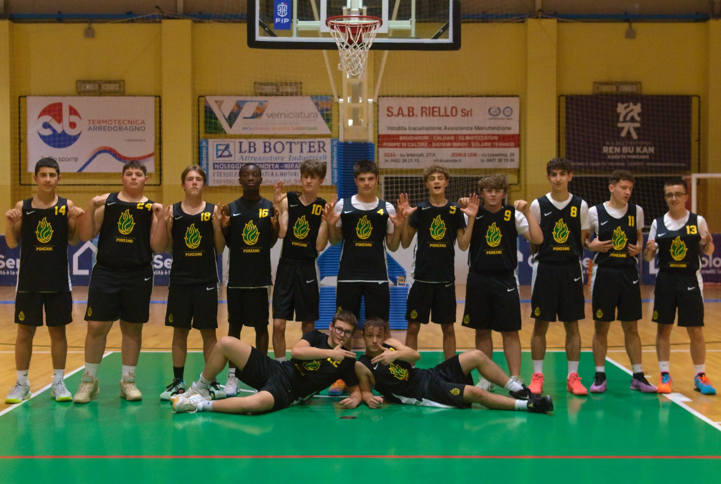 Squadra di basket under 17 maschile nel Palacicogna, con magliette nere con logo pallacanestro ponzano, alcuni ragazzi sono in piedi e due sono sdraiati a terra in primo piano.