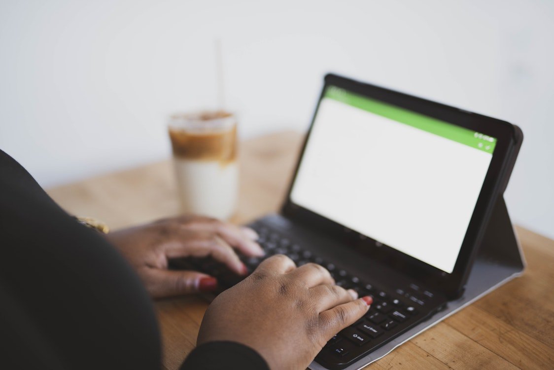 Person typing on a small laptop with a glass of iced coffee in the background.