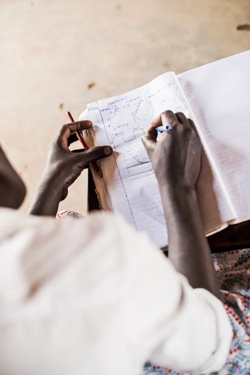 Person writing or drawing in a notebook with sketches or diagrams, using a red pen with a blue marker in hand.