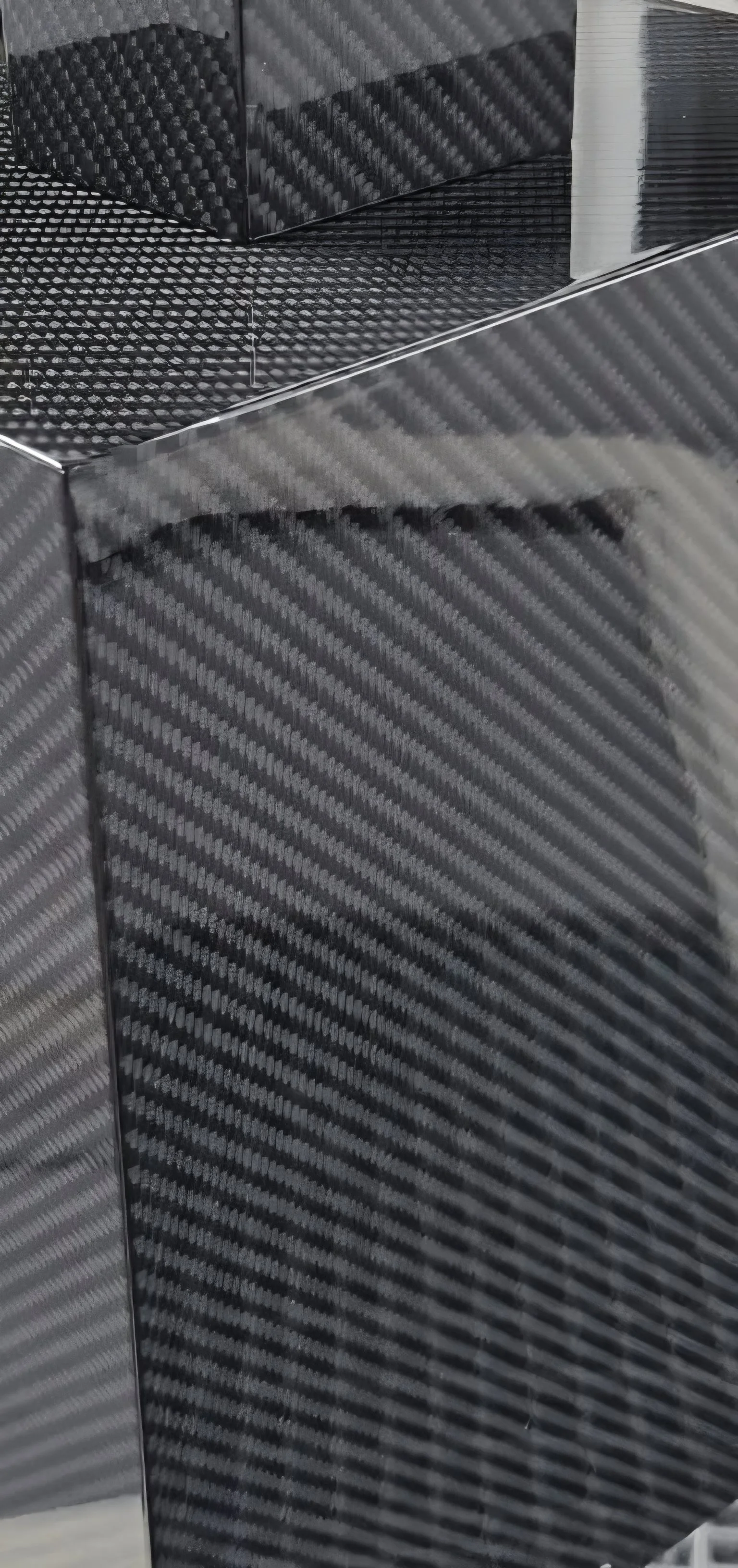 Close-up of a stack of black carbon fiber sheets with a diagonal striped pattern, showing reflective surface and edges.