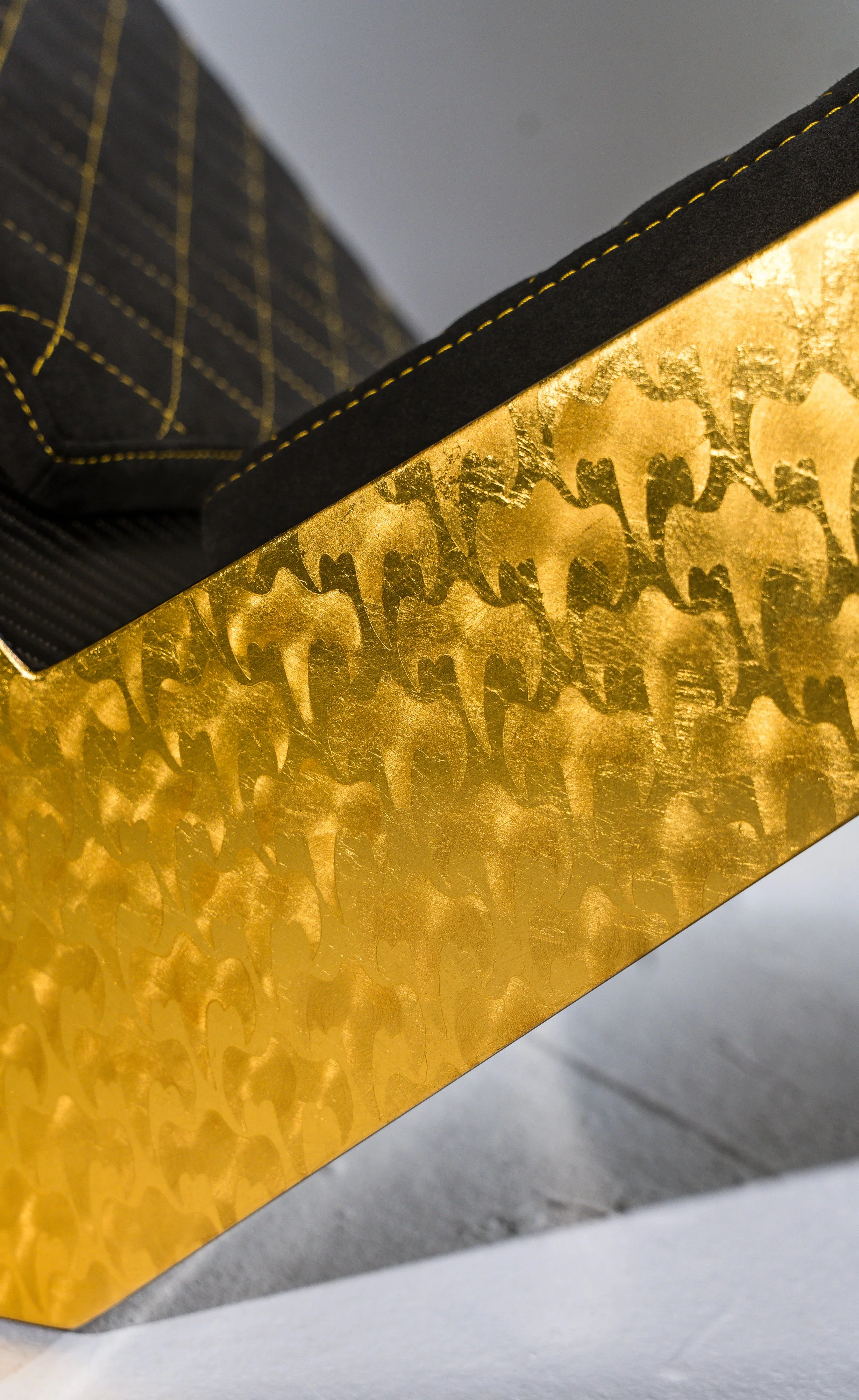 Close-up of a gold-colored box with Batman logo pattern, containing black fabric with yellow stitching.