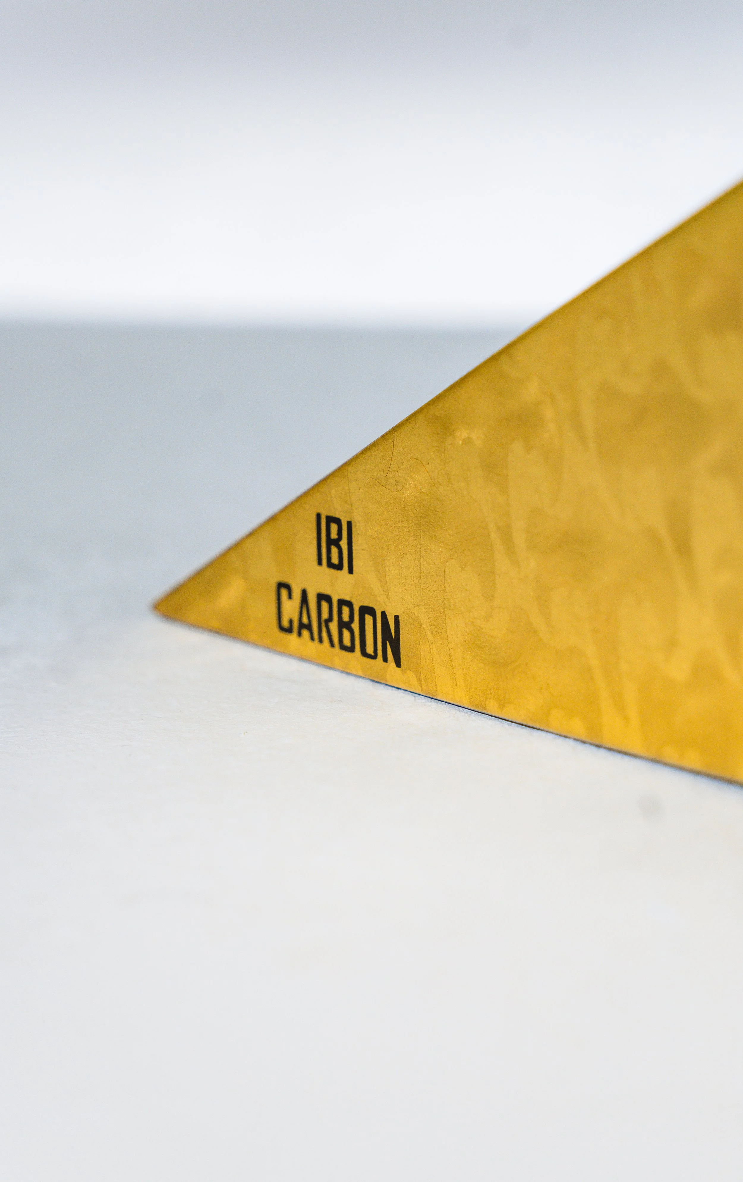 Close-up of a yellow triangular sign with the words 'IBI CARBON' printed on it, placed on a white surface.