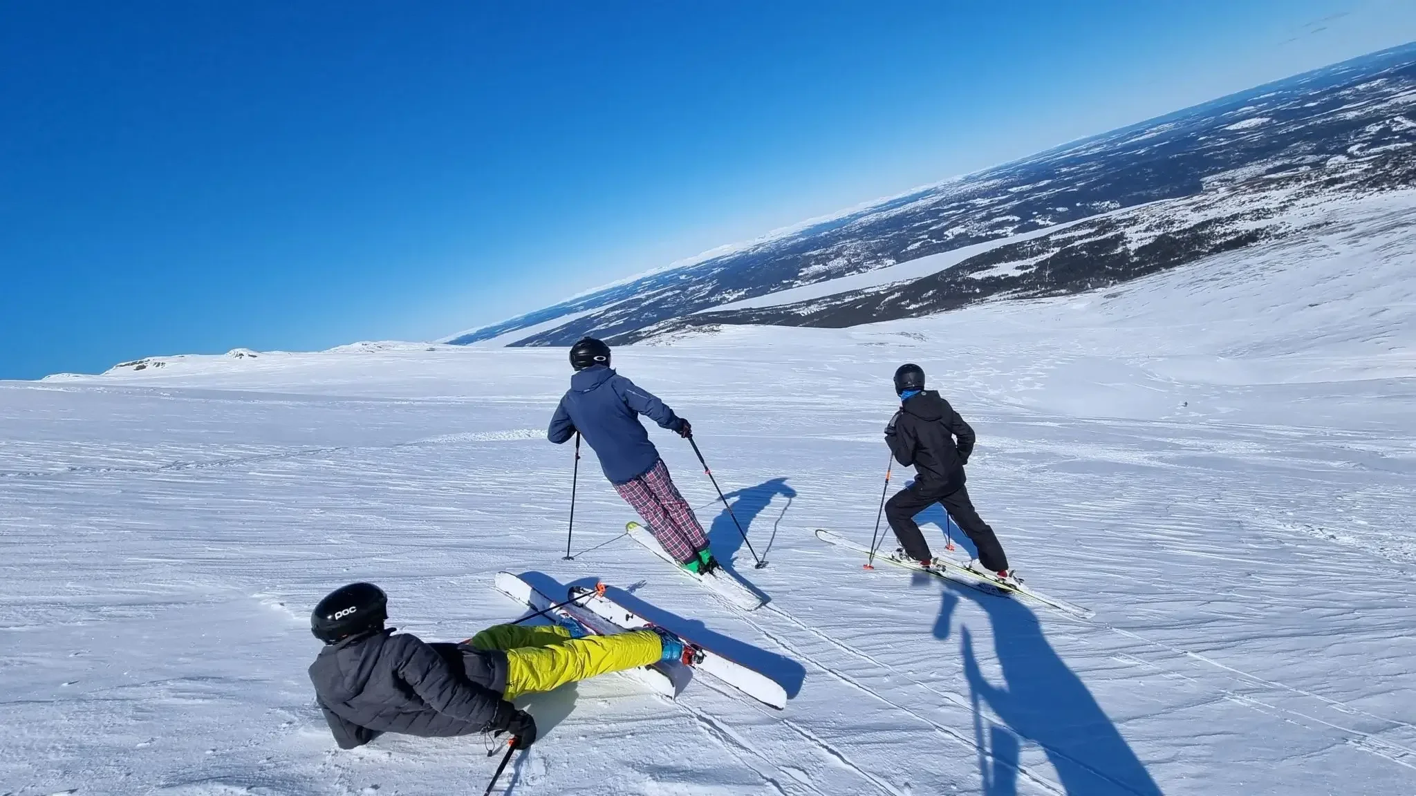 Tre skidåkare på en vidsträckt, snötäckt fjällsluttning i Huså under en klarblå himmel.