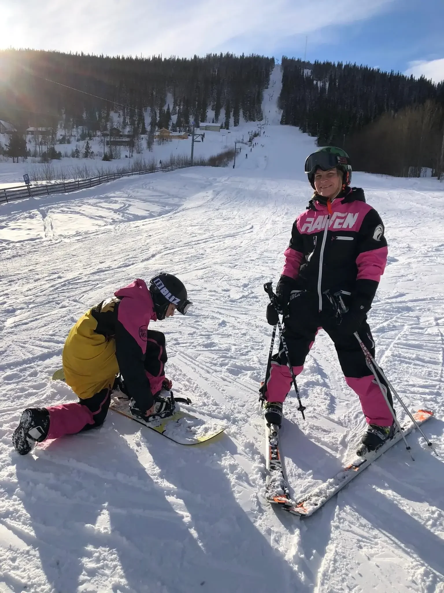En skidåkare och en snowboardåkare i matchande kläder förbereder sig i en snötäckt backe i Huså intill prislistan för skiduthyrning.