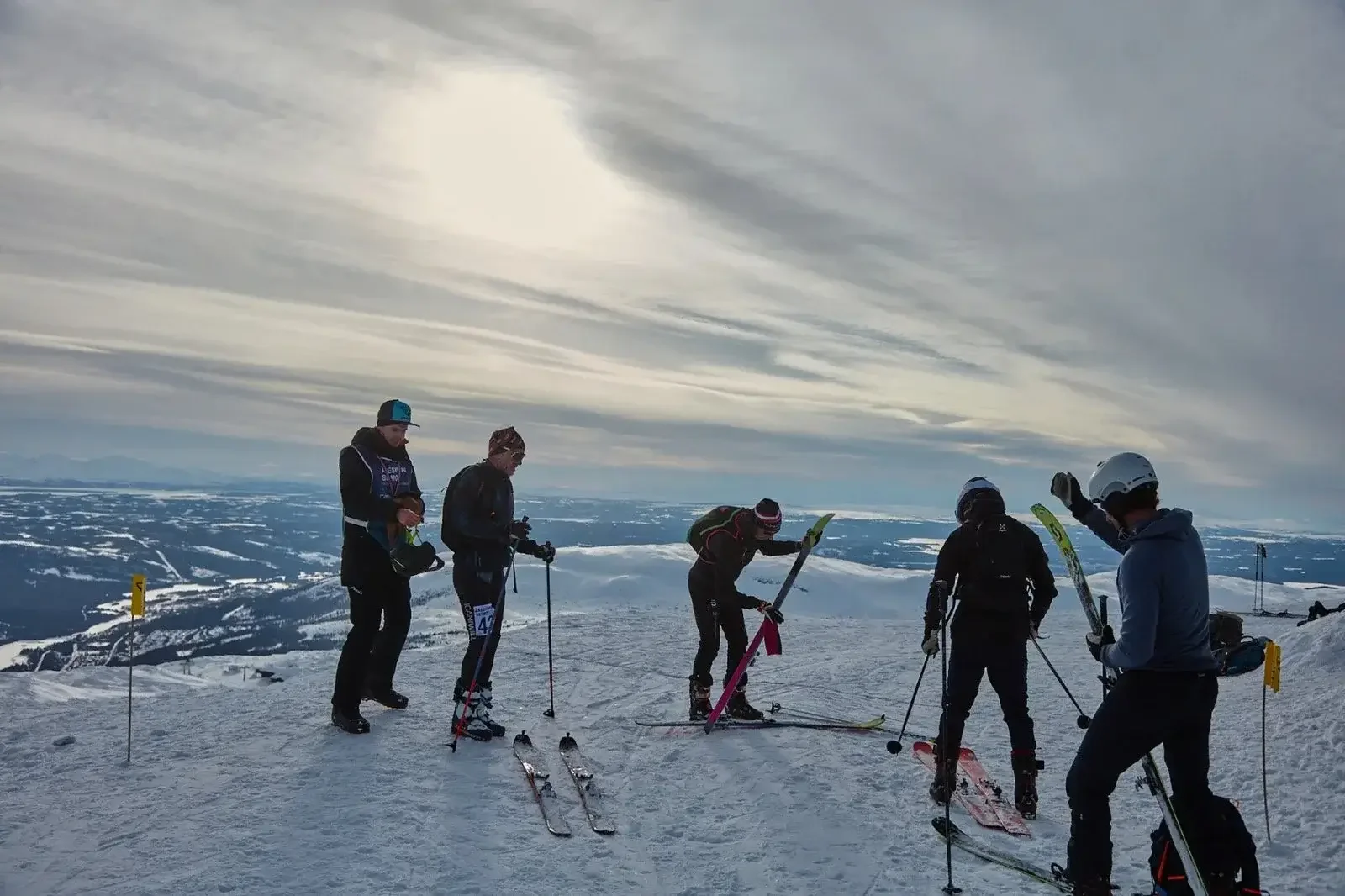 En grupp skidåkare förbereder sig på en snöig fjälltopp med vidsträckt utsikt.