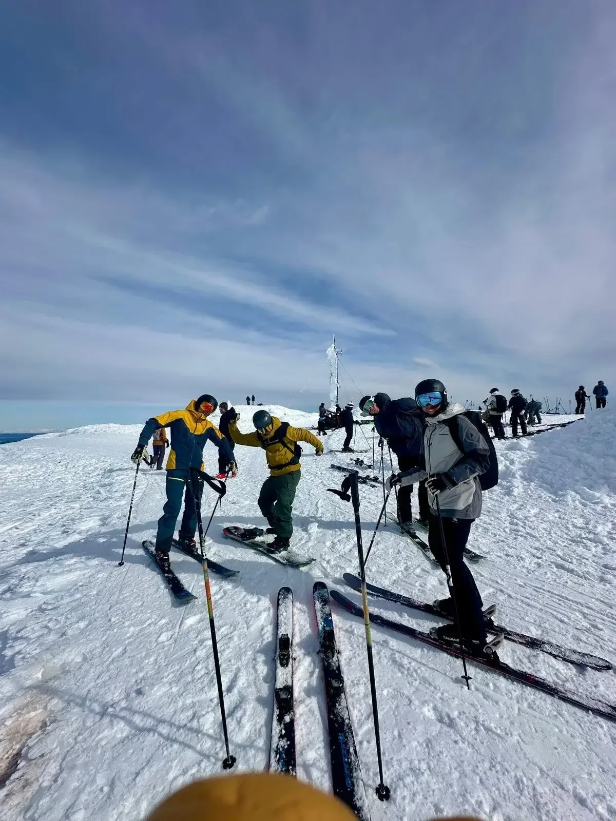 En grupp skidåkare och snowboardåkare som samlas på en snöig bergstopp.