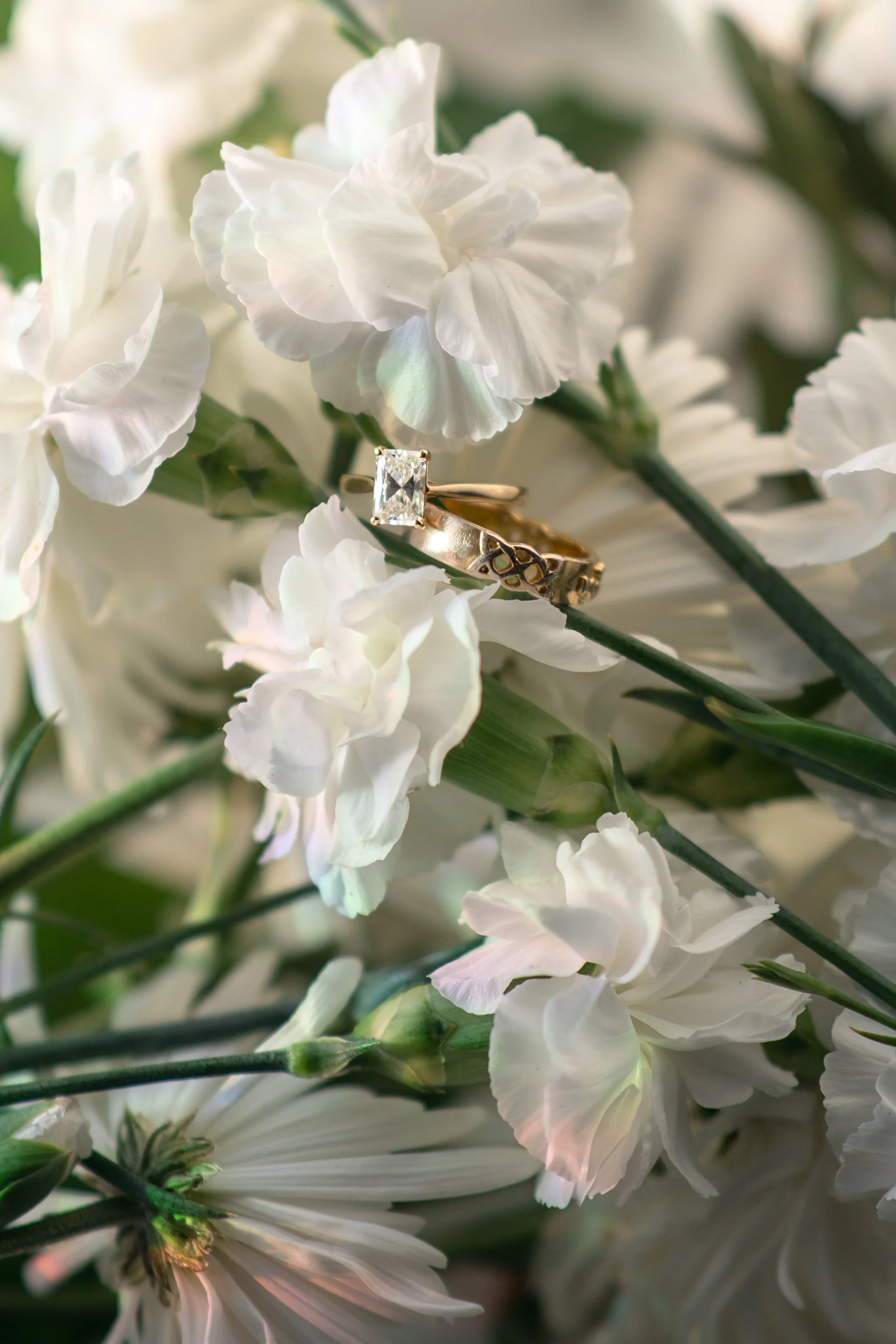 White flowers with an engagement ring featuring a large rectangular diamond resting on one of the petals.