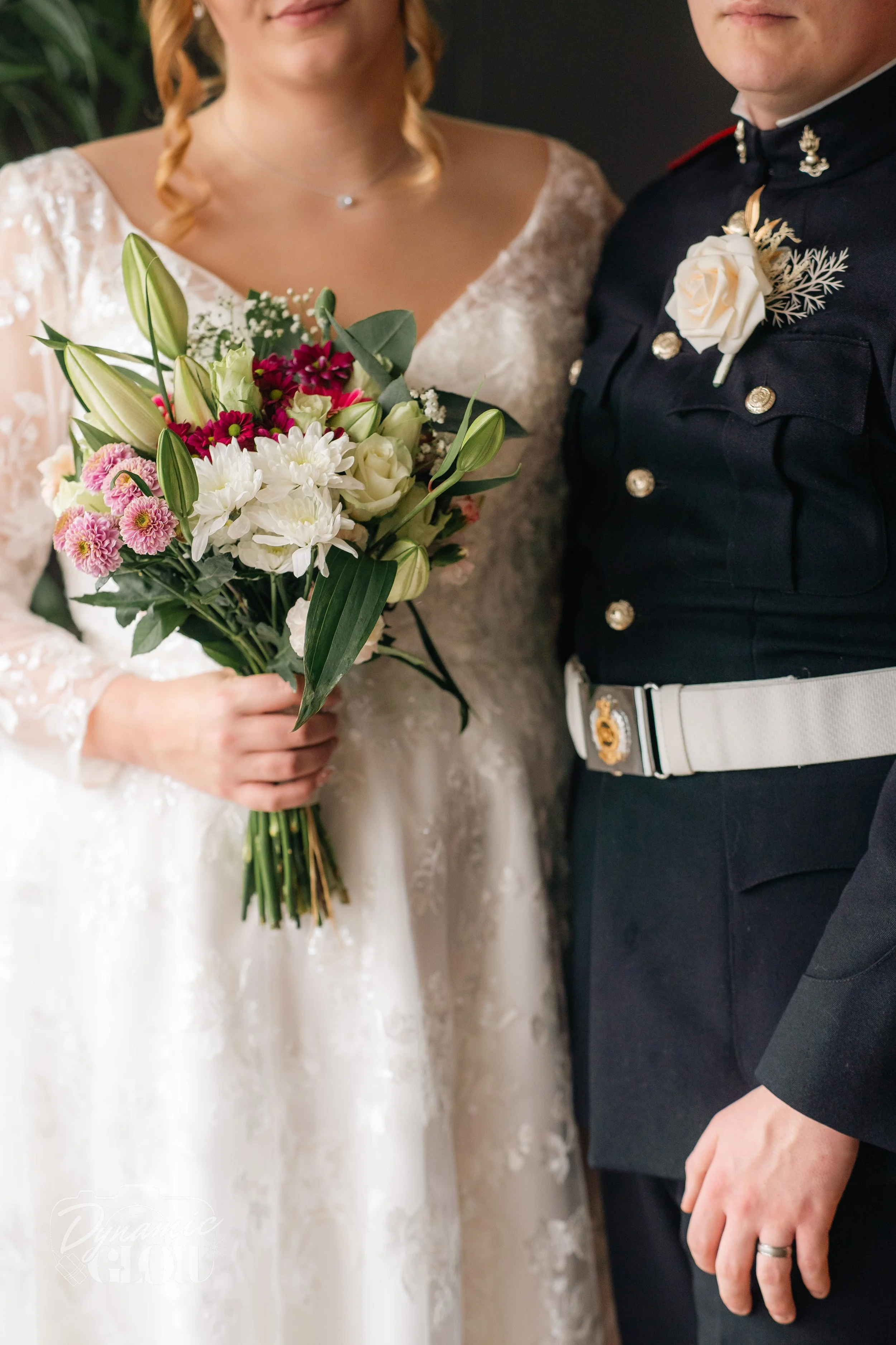 A bride holding a bouquet of white, pink, and purple flowers standing next to a groom in a military uniform.