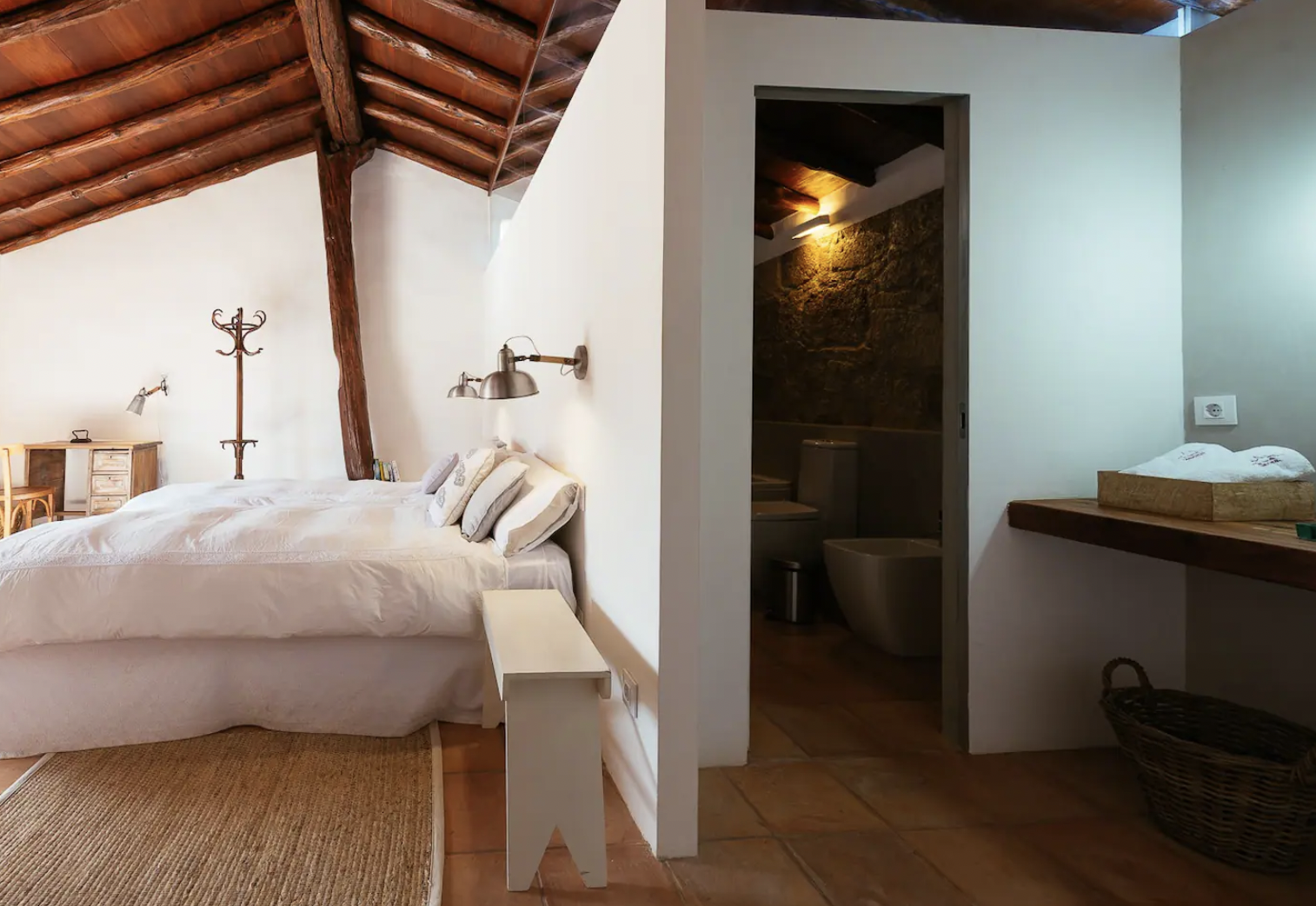 Rustic bedroom with a wooden ceiling, double bed, white bedding, and adjacent bathroom.