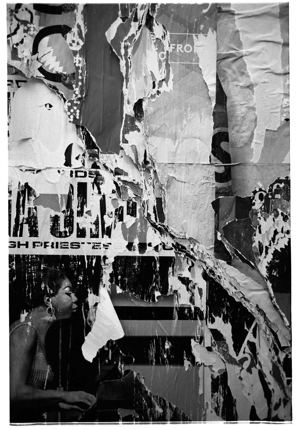 A black and white photograph of a torn and layered poster featuring a woman playing the piano, wearing earrings and a patterned dress, with partial text and images visible in the background.