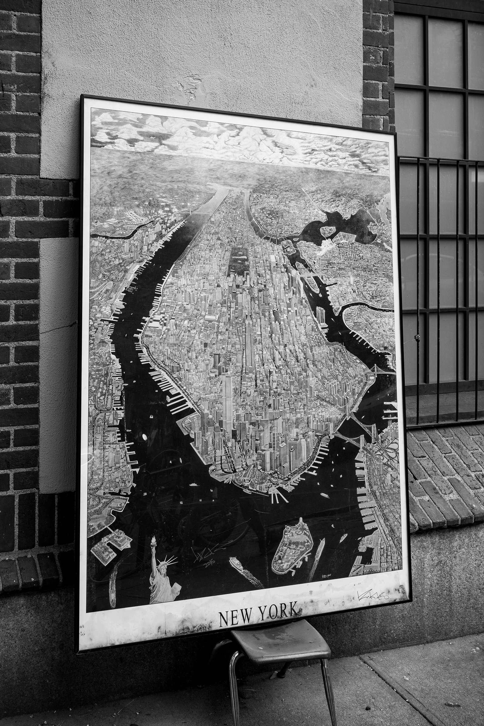 Black and white aerial map of New York City showing waterways, buildings, and landmarks, with a small Statue of Liberty illustration at the bottom left.