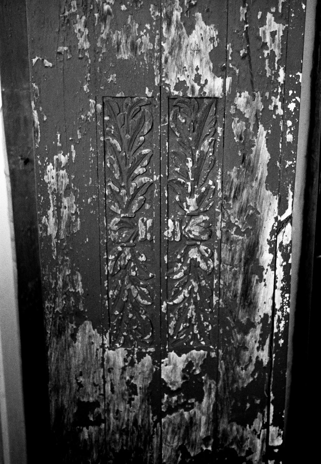 A black and white photo of a worn wooden door with peeling paint and carved decorative patterns in the center.
