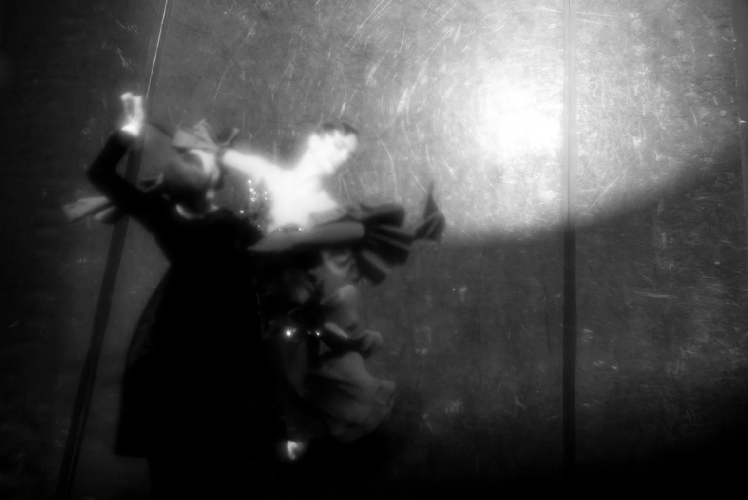 A black and white photograph of a woman lying on the ground, with wet hair and dressed in dark clothing, illuminated by a bright light source.