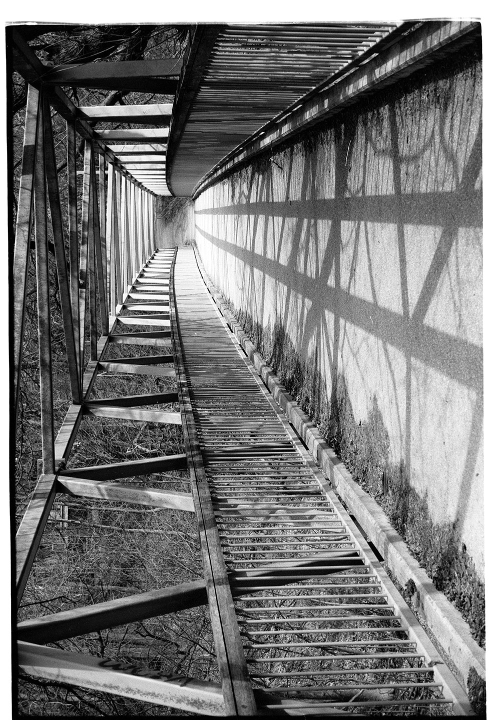 Black and white photo of a tall metal fire tower structure with stairs and railings, casting shadows on the ground below.